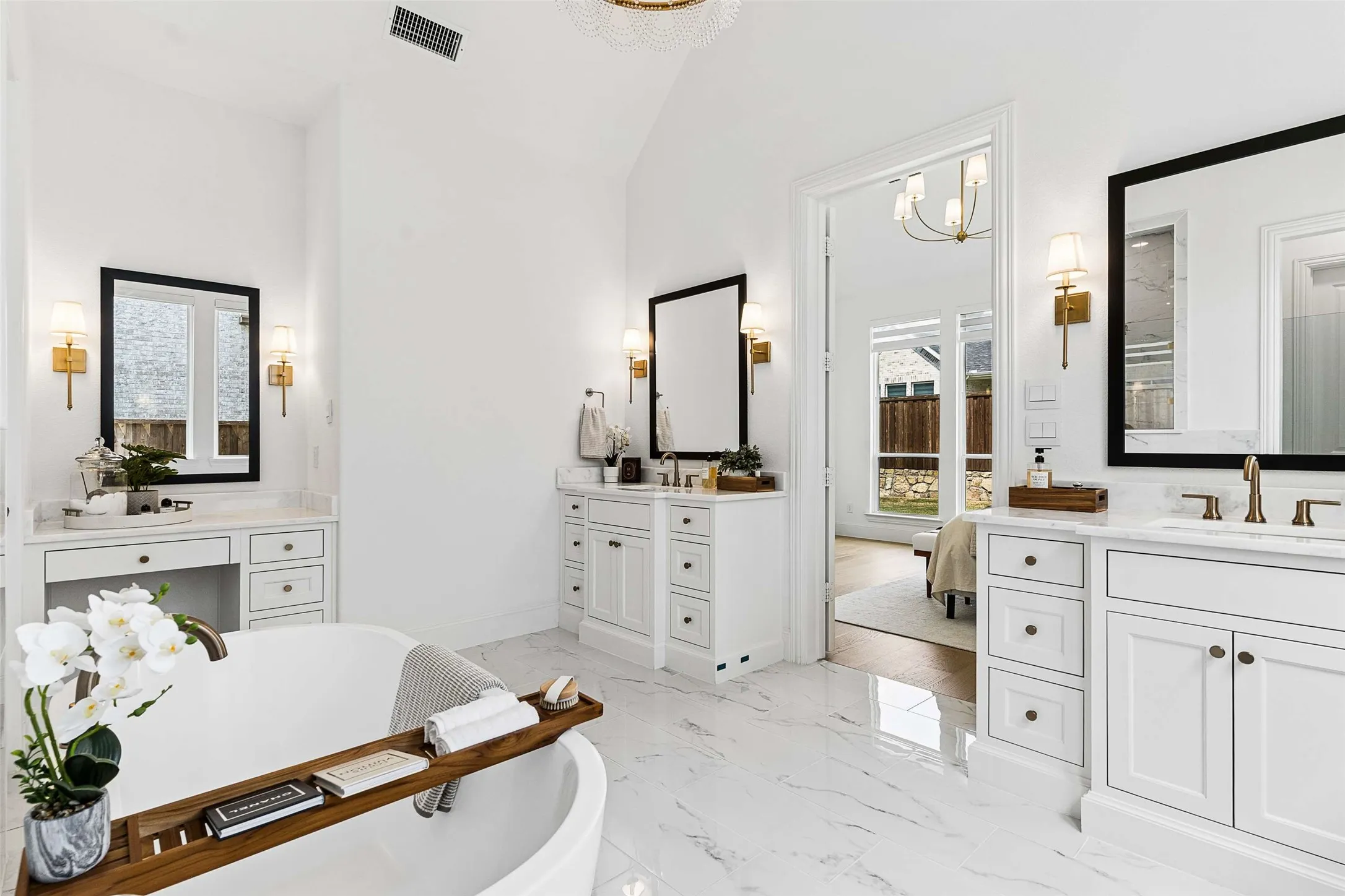 Freestanding soaking tub, white dual vanities with integrated sinks, white cabinetry with dark hardware, large framed mirrors, and marble-look tile flooring