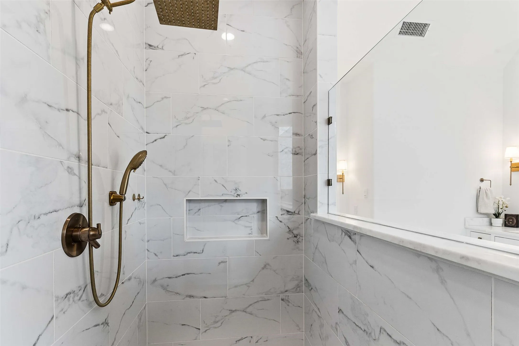 Shower featuring marble-look tile, a built-in shower niche, and a bronze-finish shower system with a handheld spray and rain shower head