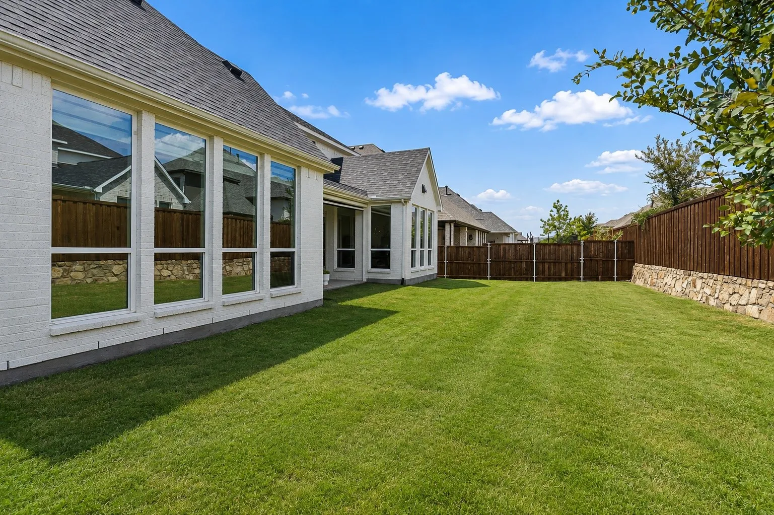 Expansive green lawn with a privacy fence featuring a stone base