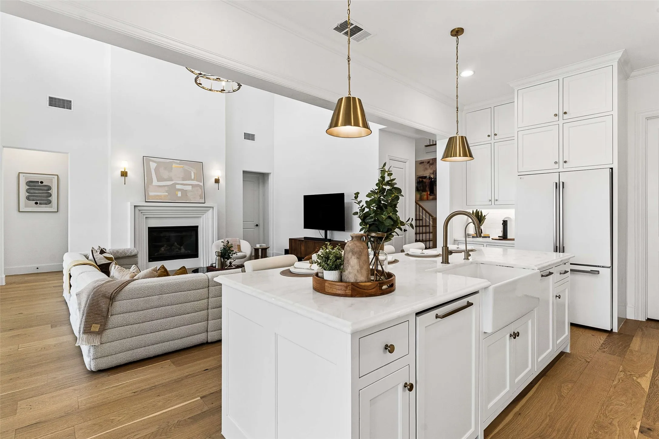 Expansive living space featuring wood-finish flooring, a white kitchen island with a farmhouse sink, and white cabinetry