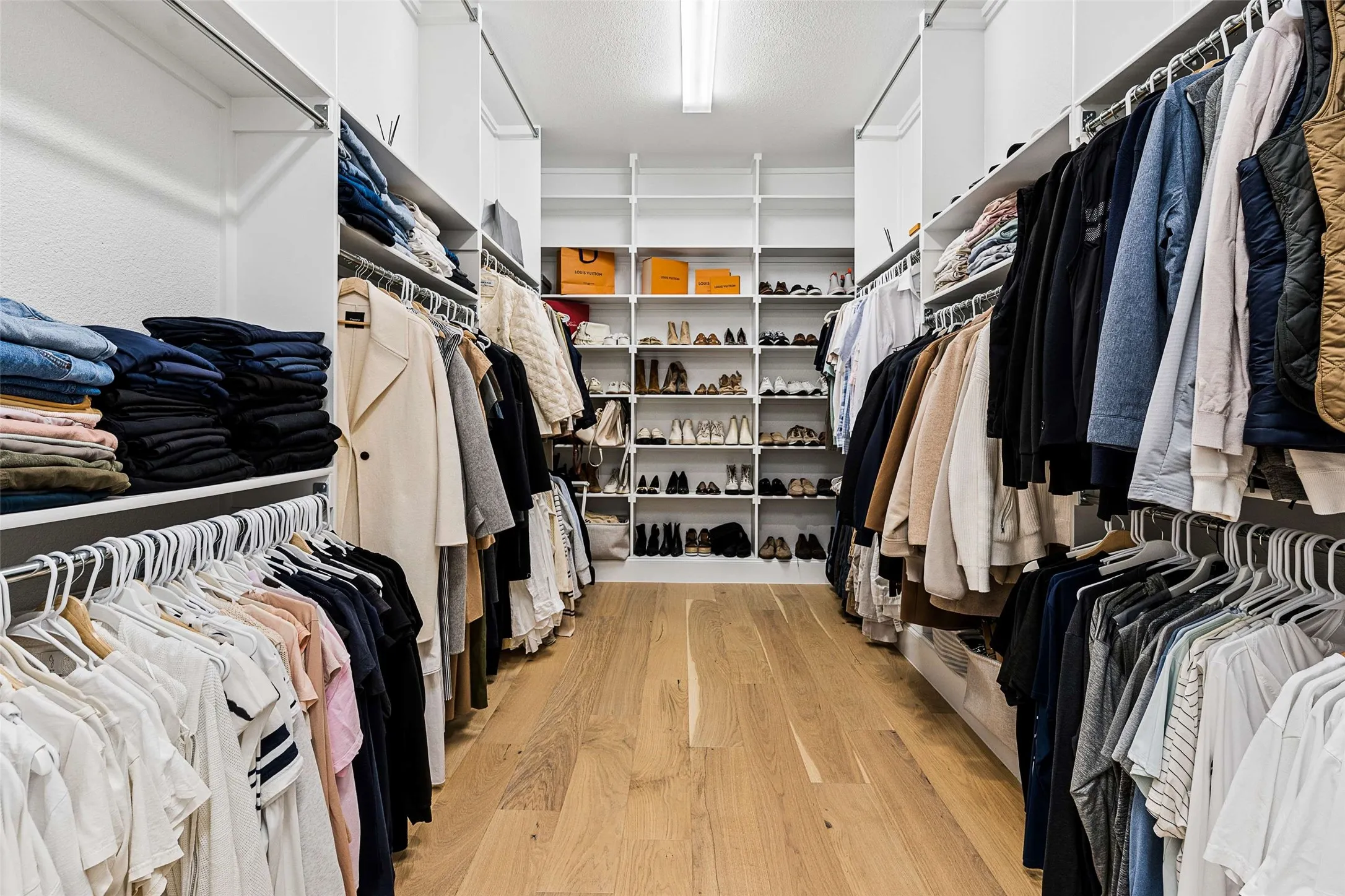 Walk-in closet featuring wood-finish flooring, recessed lighting, built-in shelving, and multiple hanging rods for organization