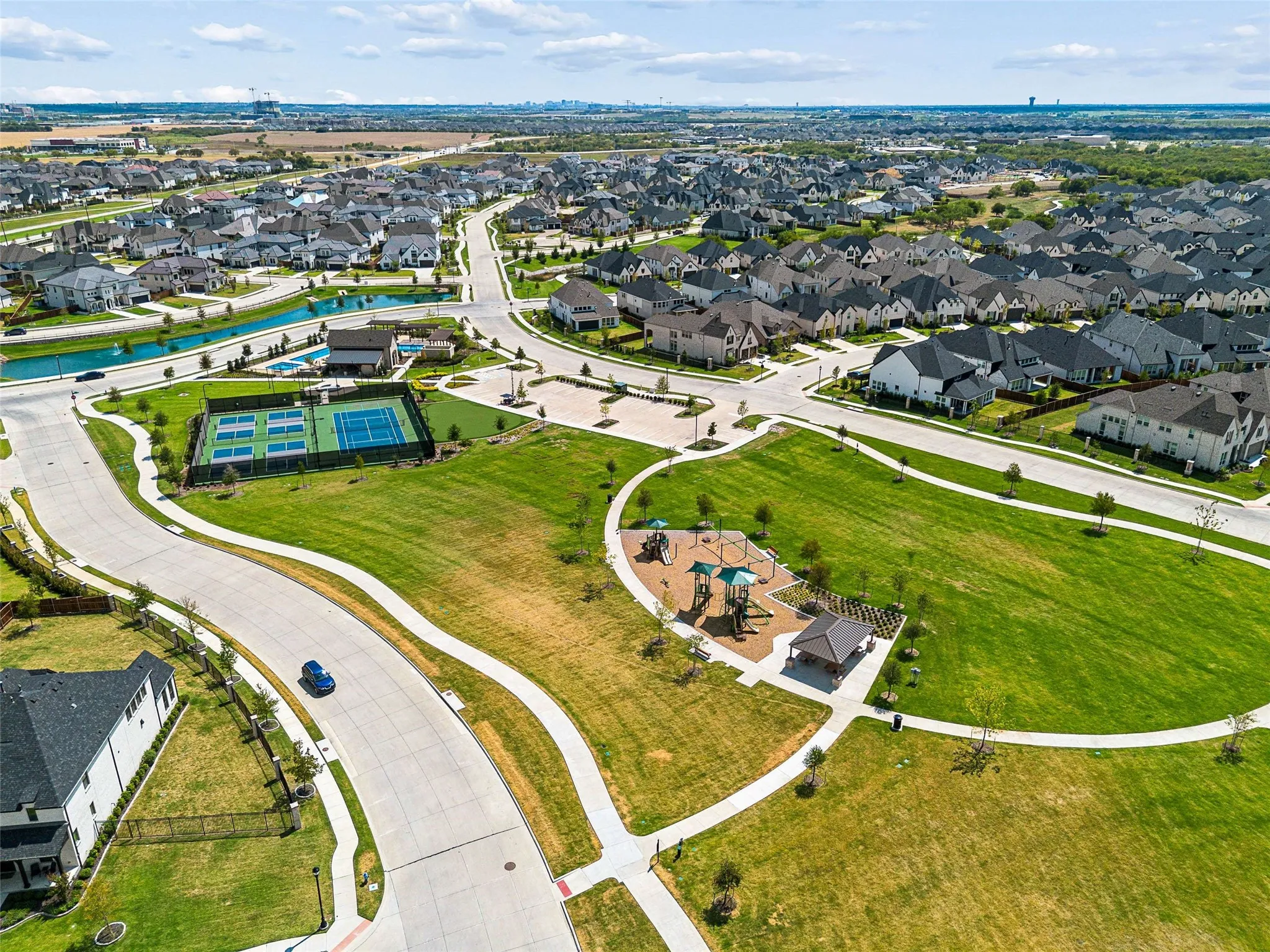 Expansive green spaces featuring walking paths, a playground structure, and an amenity center with tennis courts and a swimming pool