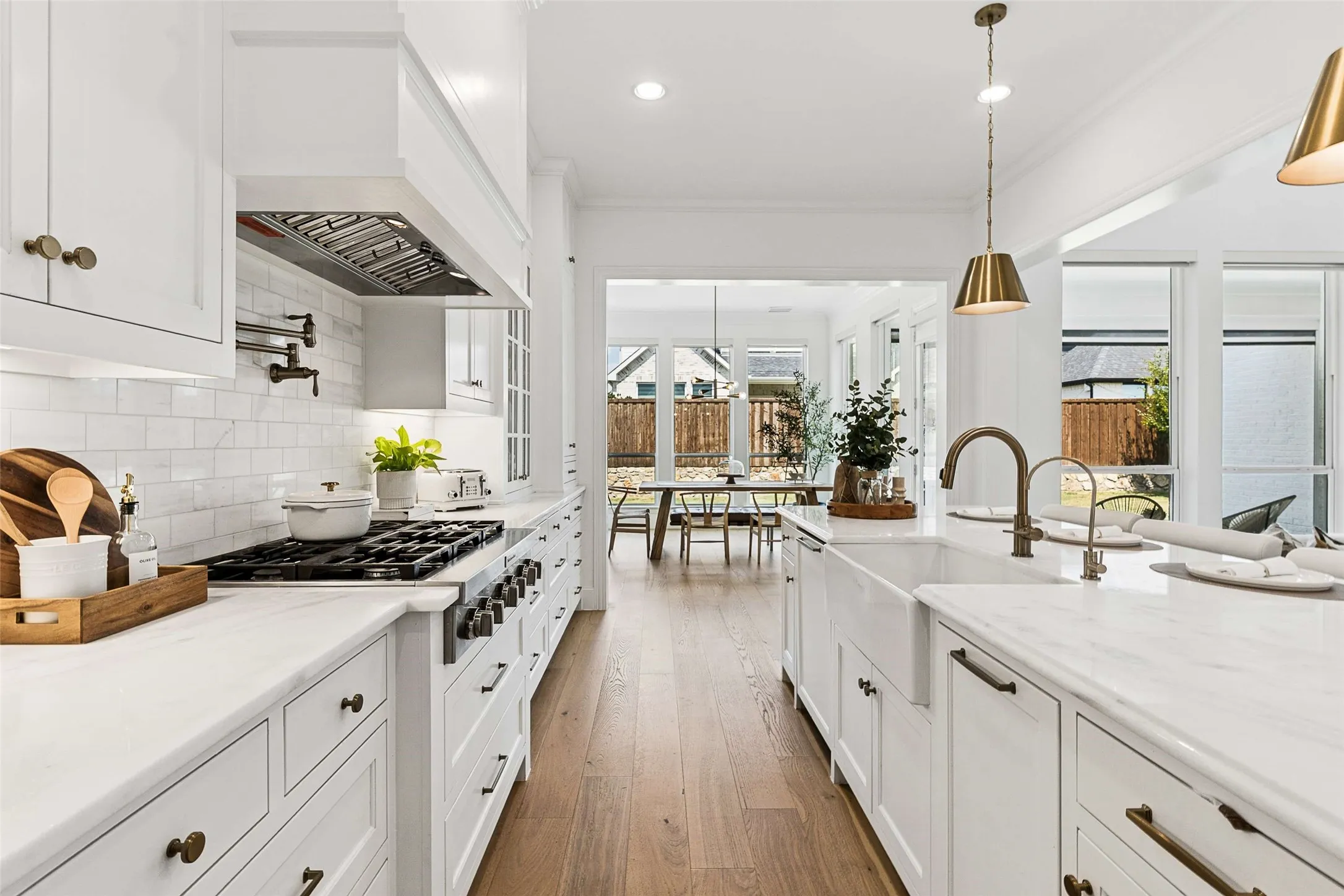 White shaker cabinetry, wide plank wood-finish flooring, white subway tile backsplash, white farmhouse sink, and a stainless steel range with a pot filler