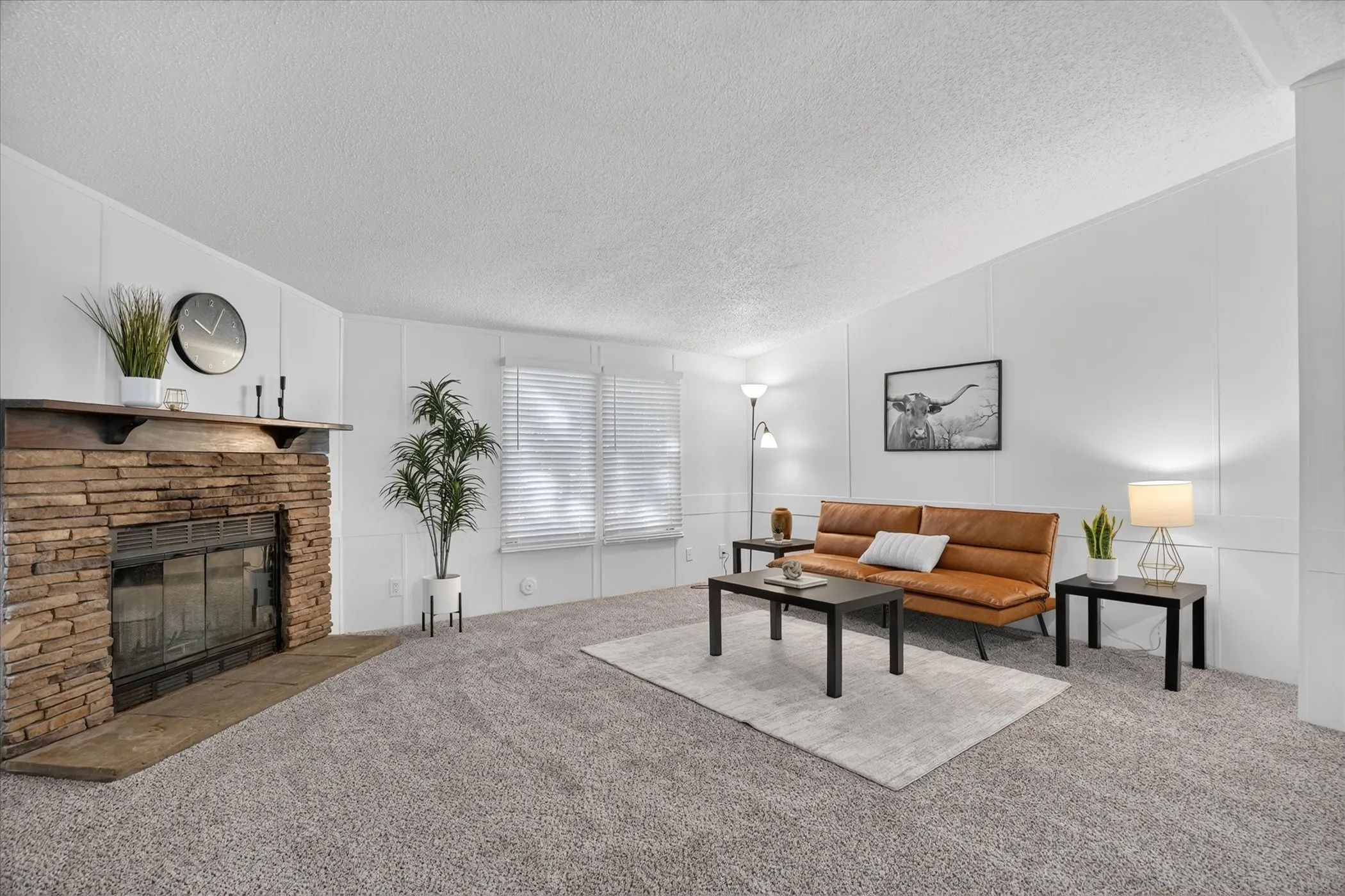 Spacious room featuring a stone-clad fireplace with wood mantle, light gray carpeting, and white paneled walls