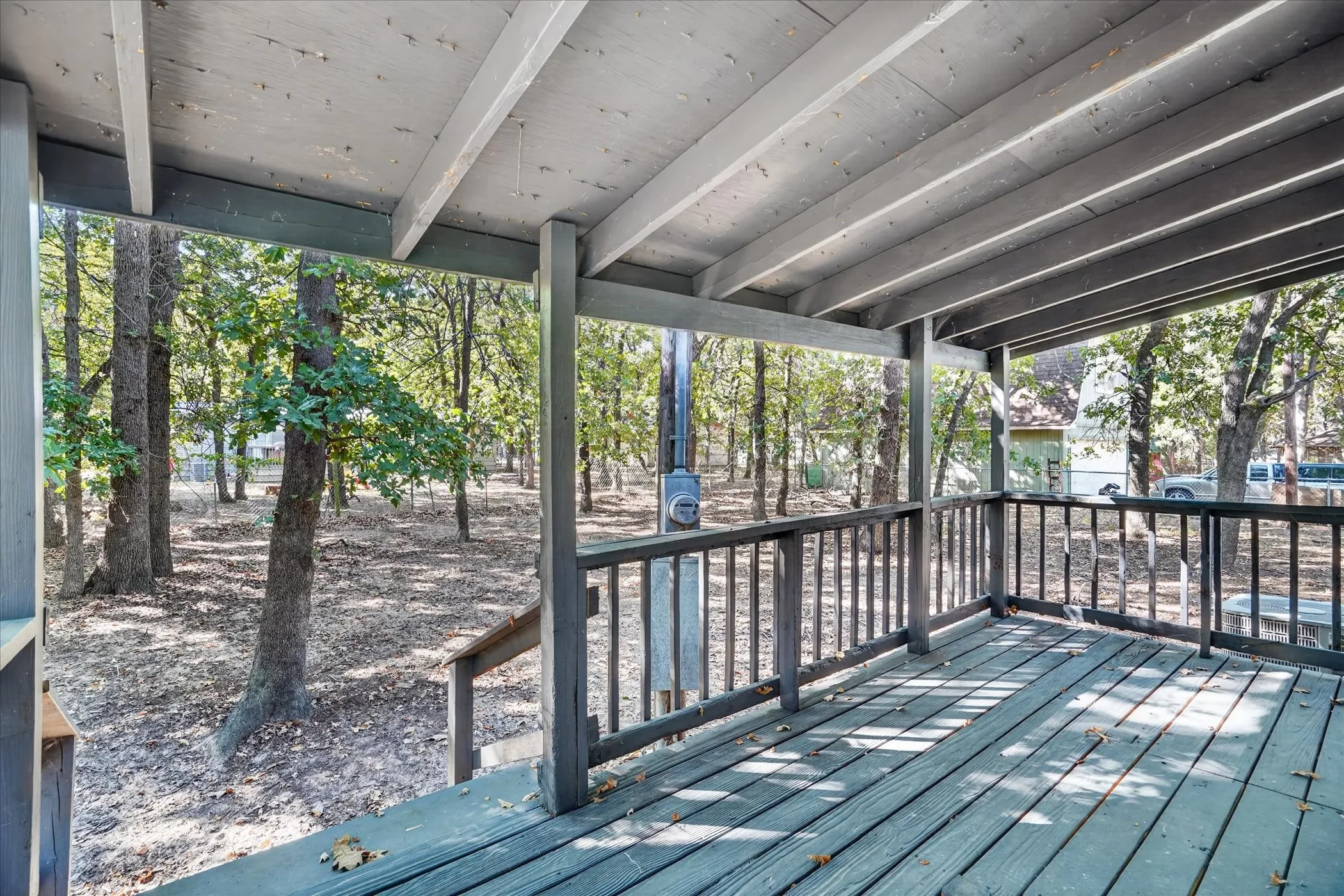 Covered porch with wood flooring and exposed ceiling beams, featuring a wood railing