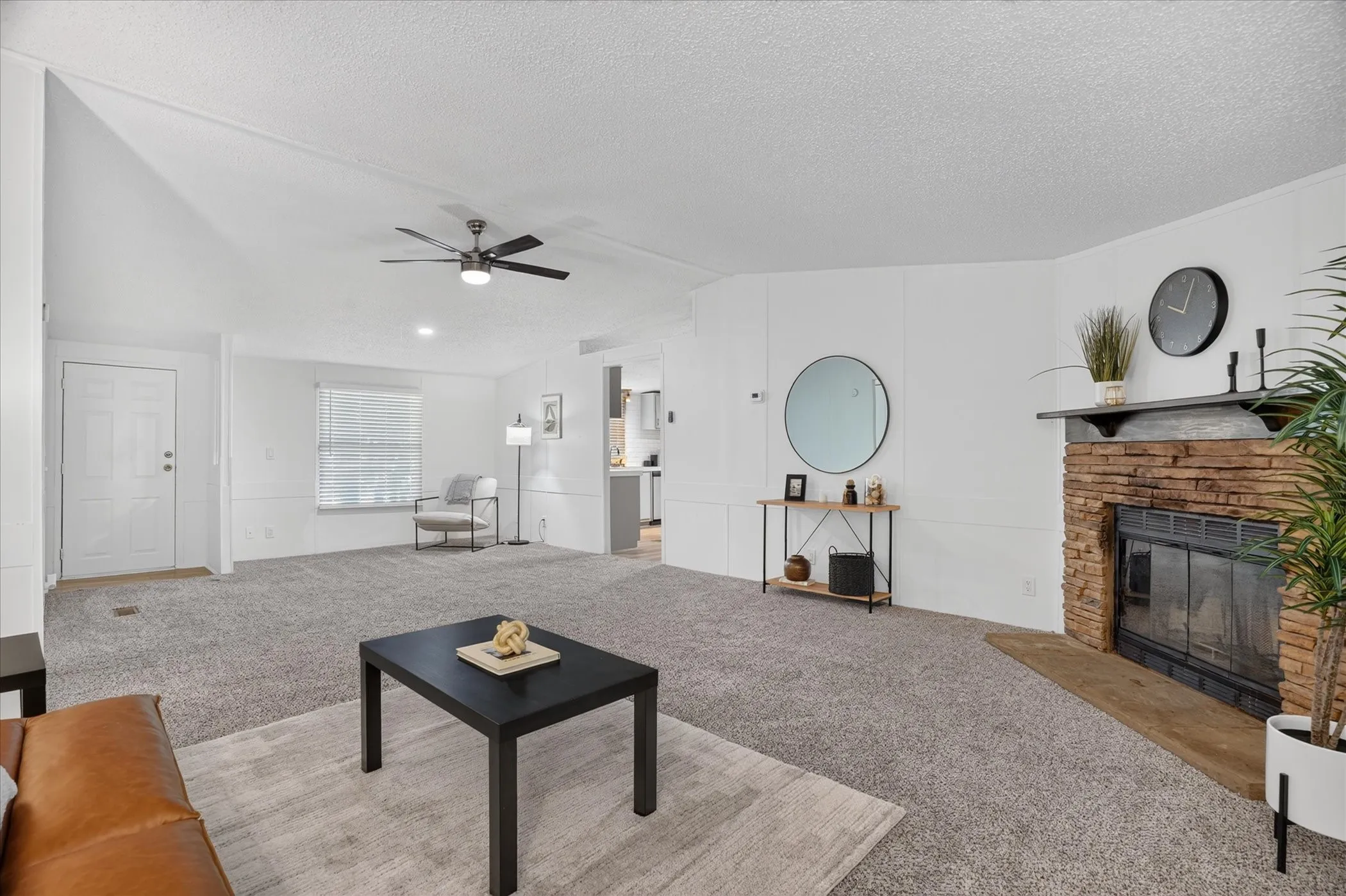 Spacious living area featuring a stone-clad fireplace, ceiling fan, and light gray carpeting