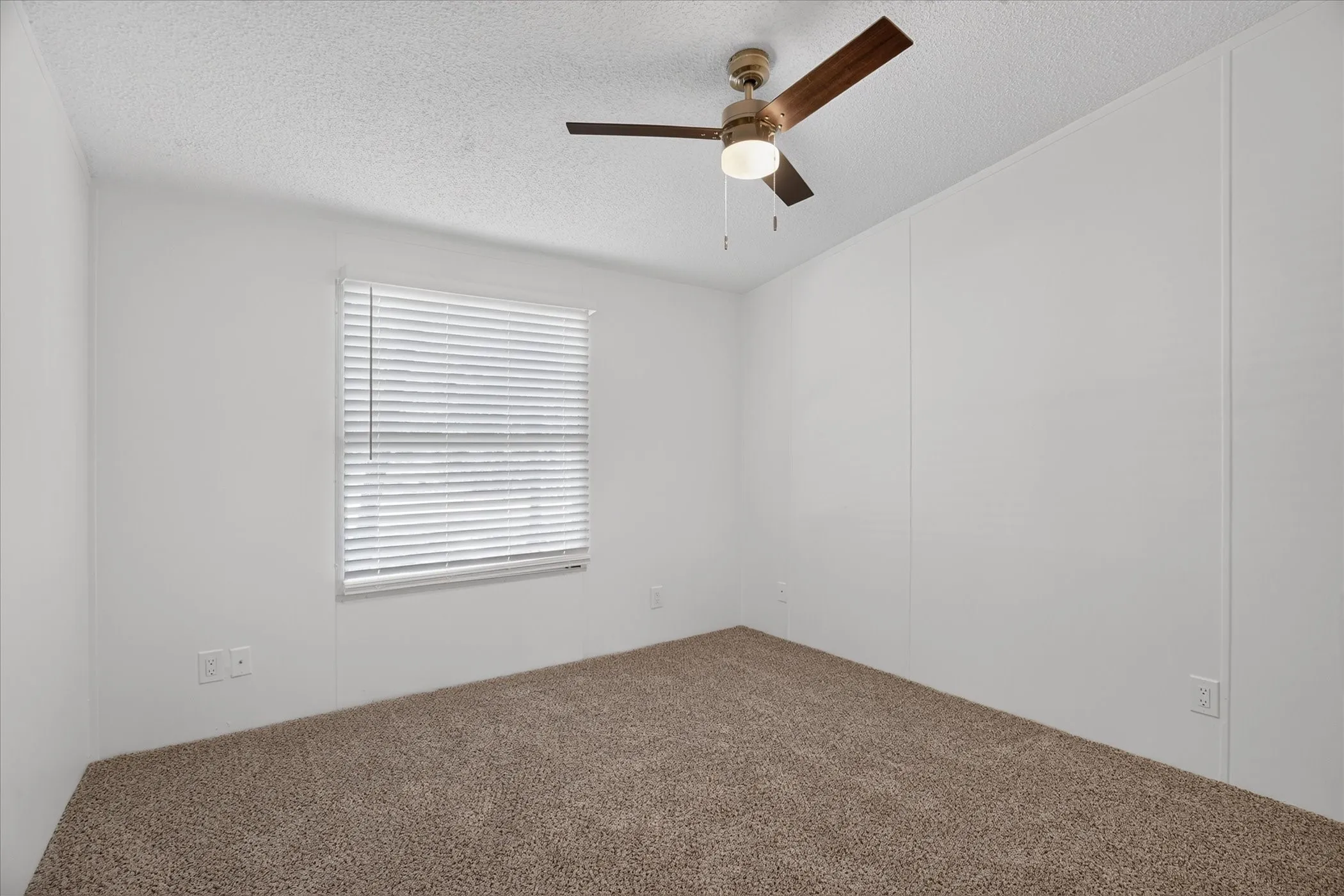 Recessed window with blinds, ceiling fan with light, and textured carpet flooring