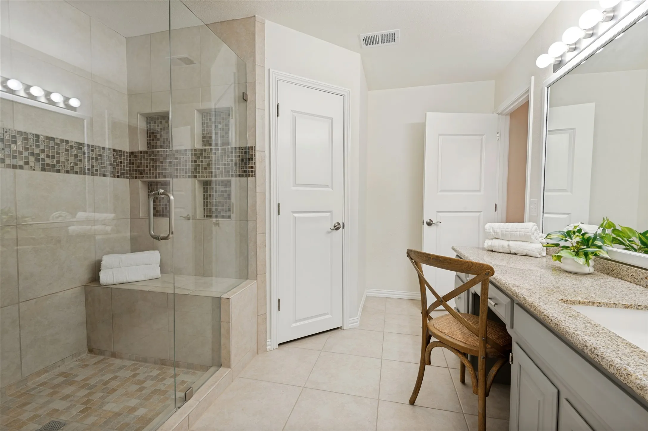 Great views of the shower "built for 2" and the shower bench seat for relaxation.  The closed door leads into 1 of the 3 walk-in closets and the open doorway directs you back into the primary bedroom.