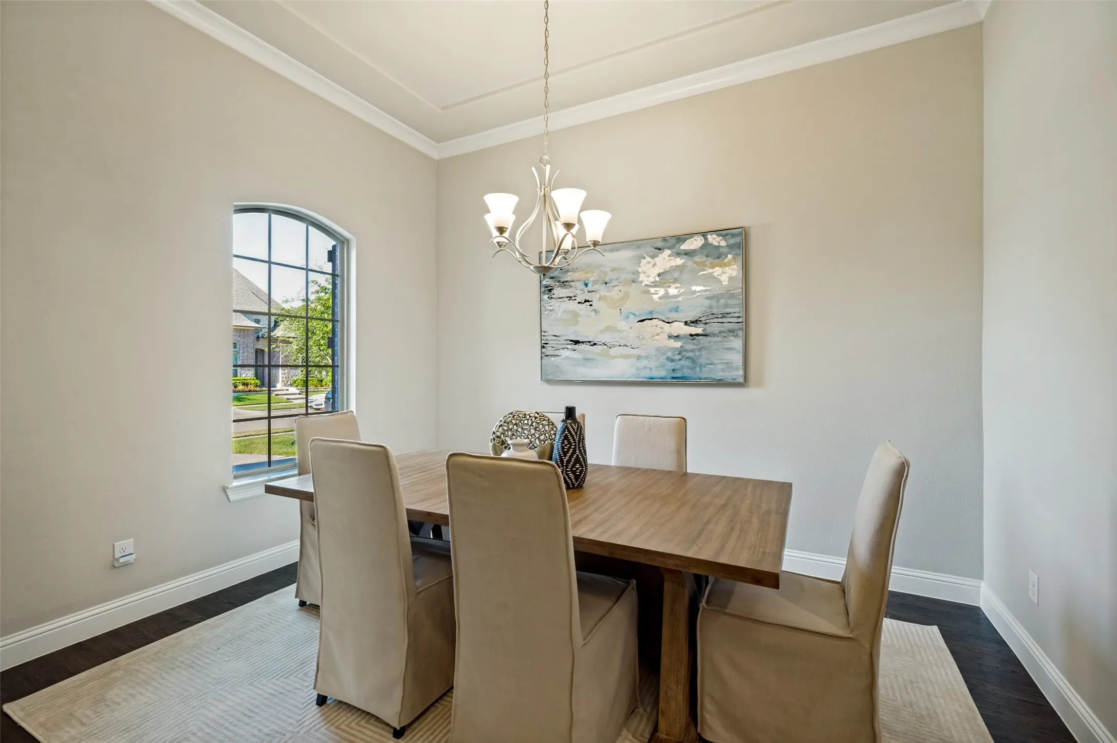 A sophisticated formal dining room sets the stage for memorable gatherings, featuring a tray ceiling, elegant chandelier, and rich hardwood floors. An arched picture window fills the space with natural light, while the spacious layout offers the perfect setting for both intima