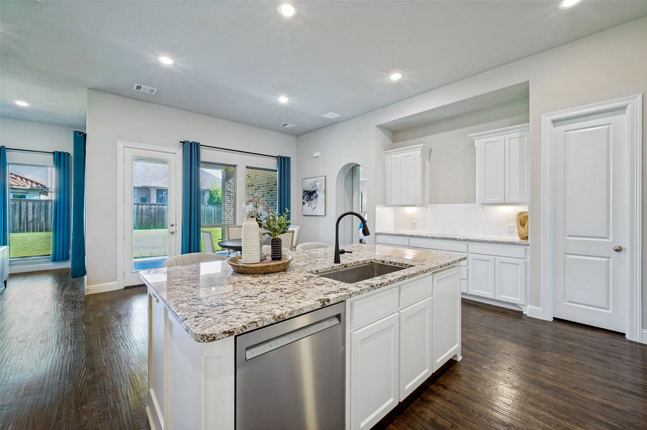 Designed for both everyday living and effortless entertaining, the chef’s kitchen is anchored by an oversized granite island with seating, abundant cabinetry, and expansive prep space. Crisp white cabinetry, a designer tile backsplash, rich hardwood floors, and seamless flow into the breakfast area create a bright, sophisticated gathering space at the heart of the home.