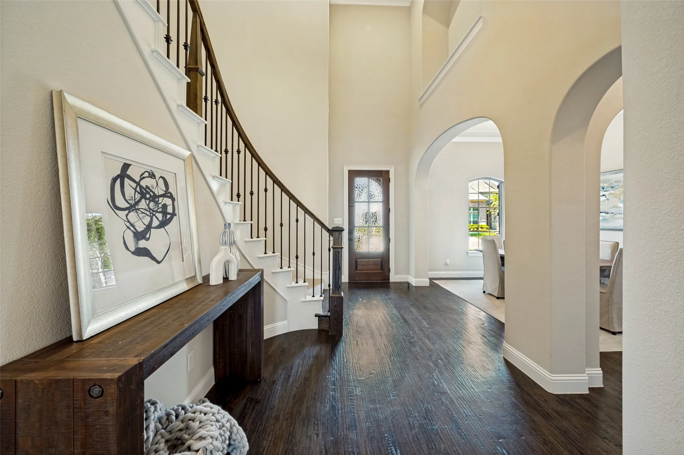 he grand entry makes a striking impression with soaring ceilings, rich hardwood floors, graceful archways, and a dramatic curved staircase with iron balusters and a stained wood handrail. Thoughtfully designed architectural details and elegant sightlines create a warm, sophisticated welcome that sets the tone for the refined interiors beyond.