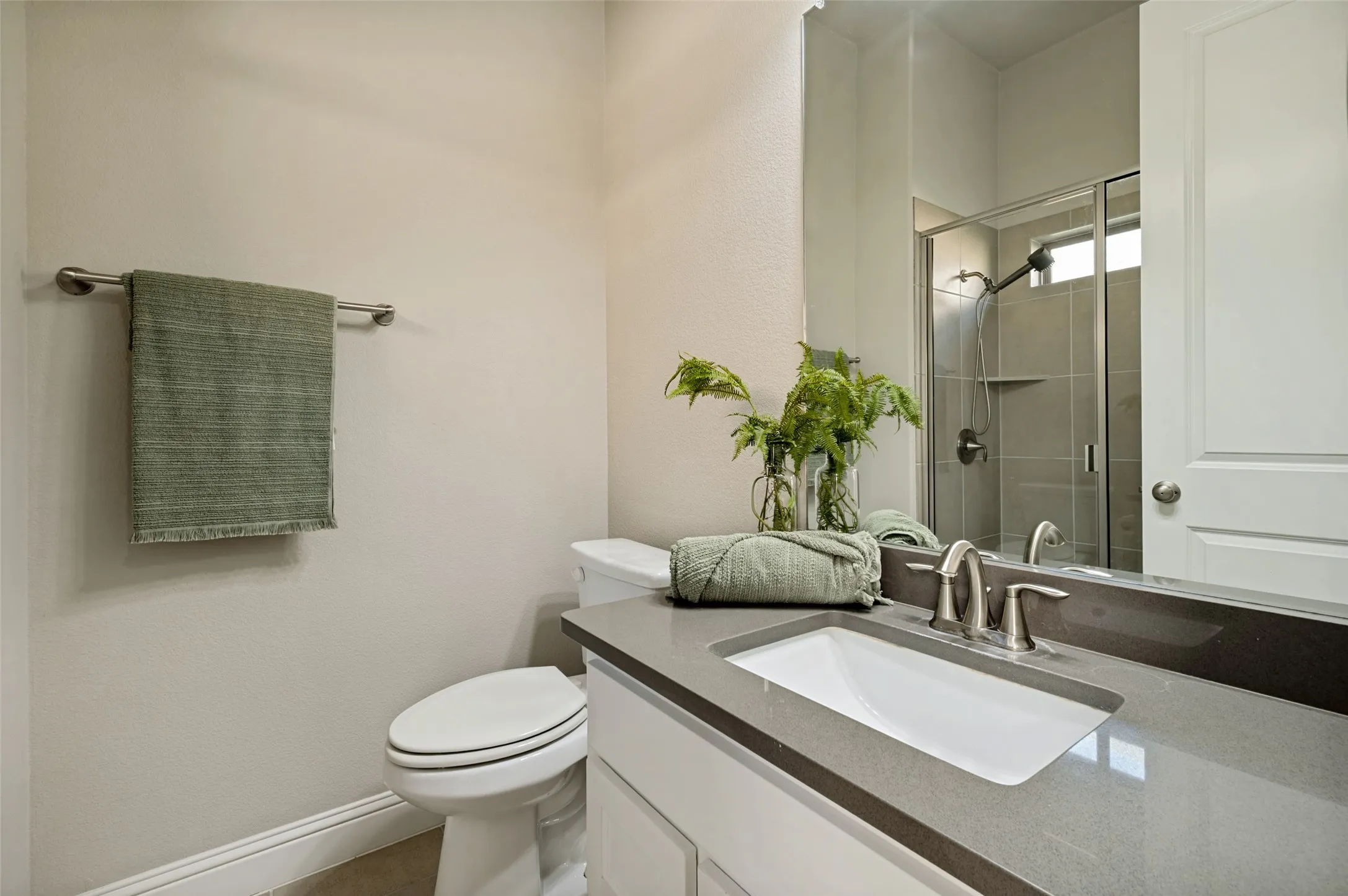 The private ensuite bath is beautifully finished with a sleek quartz vanity, framed mirror, and a spacious glass-enclosed shower with timeless neutral tile. Designed with both comfort and style in mind, it offers a polished, spa-like extension of the downstairs guest suite.