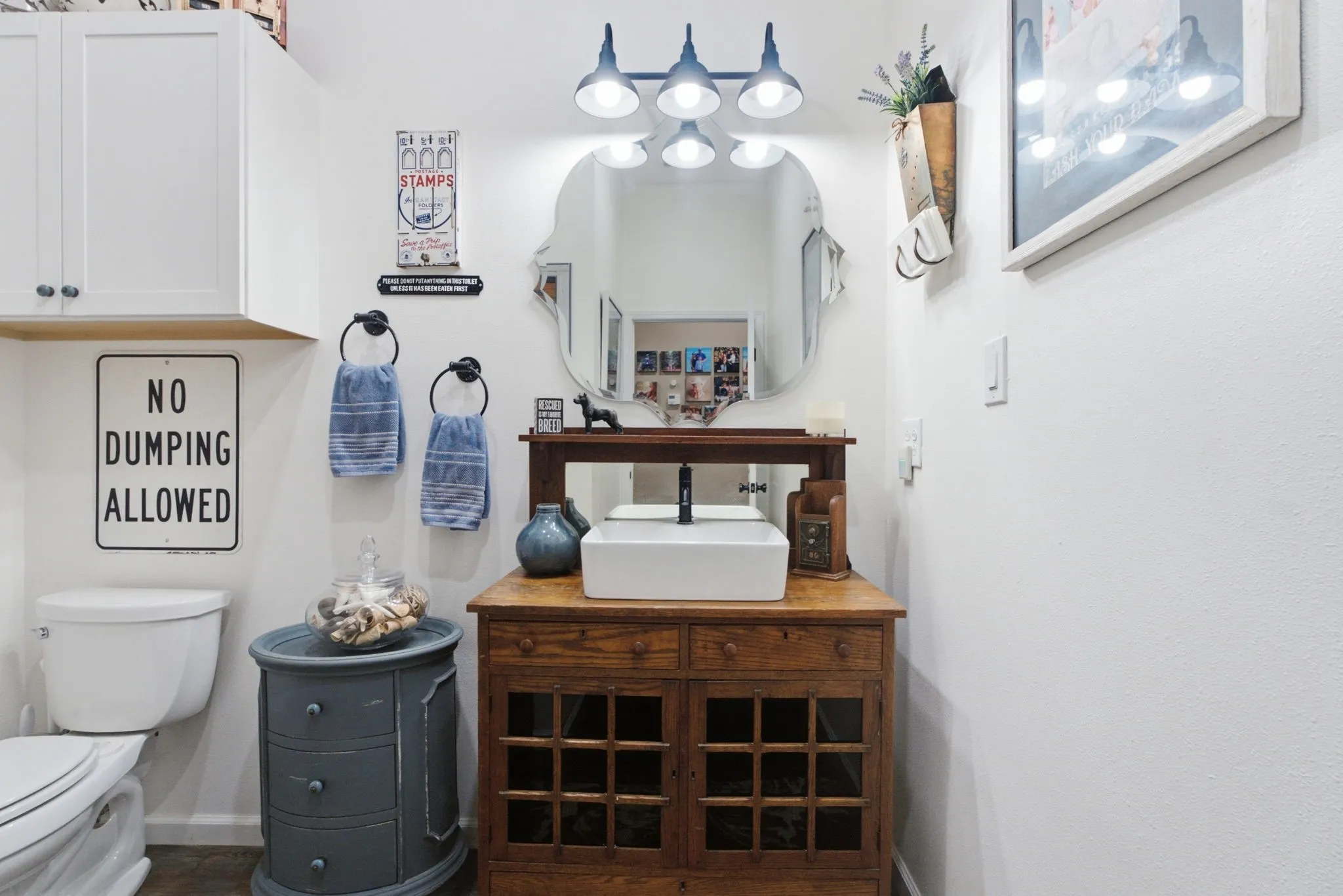 White shaker-style cabinetry, a vanity with a vessel sink, a decorative mirror, and a wall-mounted light fixture