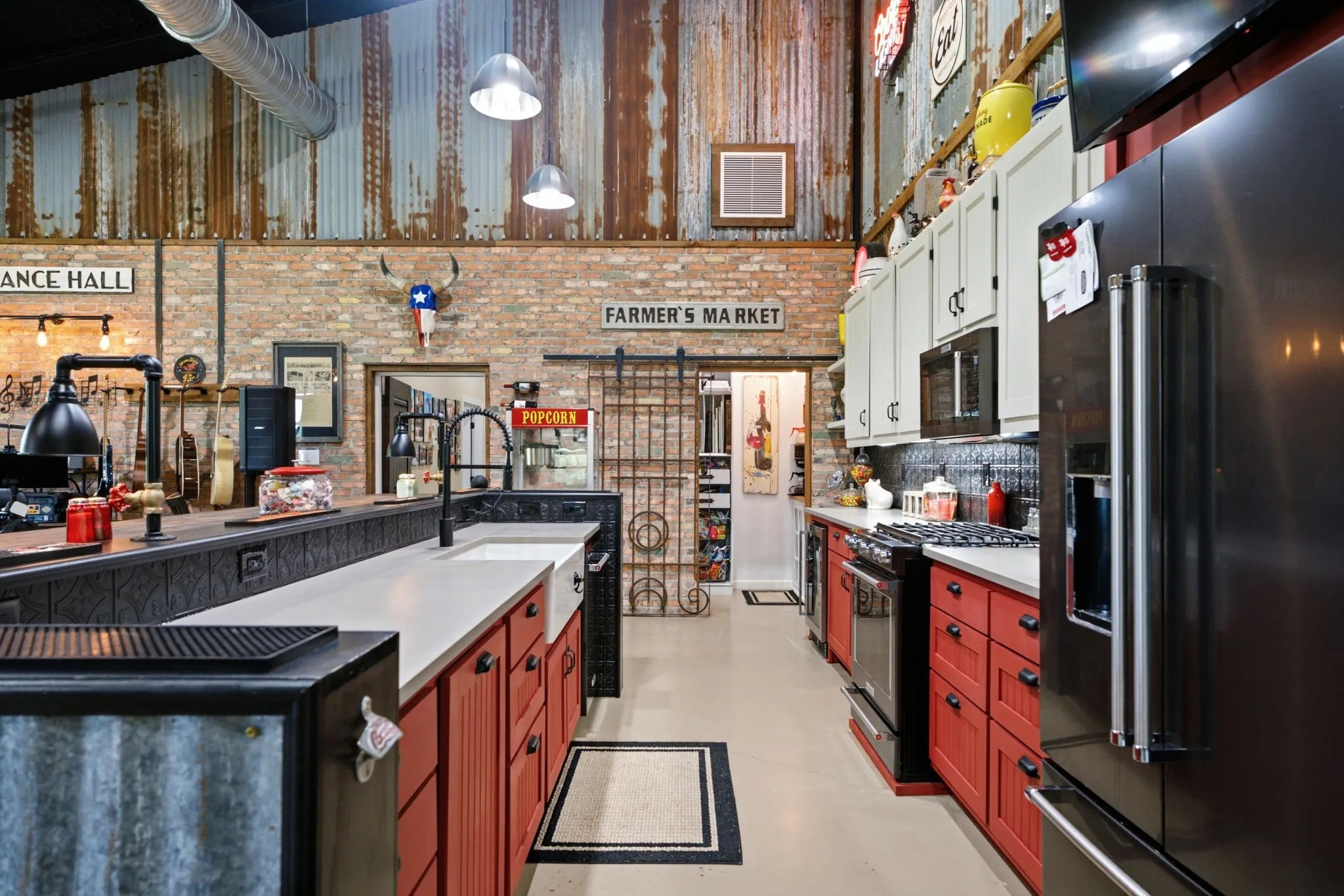 Industrial-inspired kitchen featuring red cabinetry with black countertops, stainless steel appliances, exposed brick walls with shiplap detailing, pendant lighting, and polished concrete flooring throughout the open layout