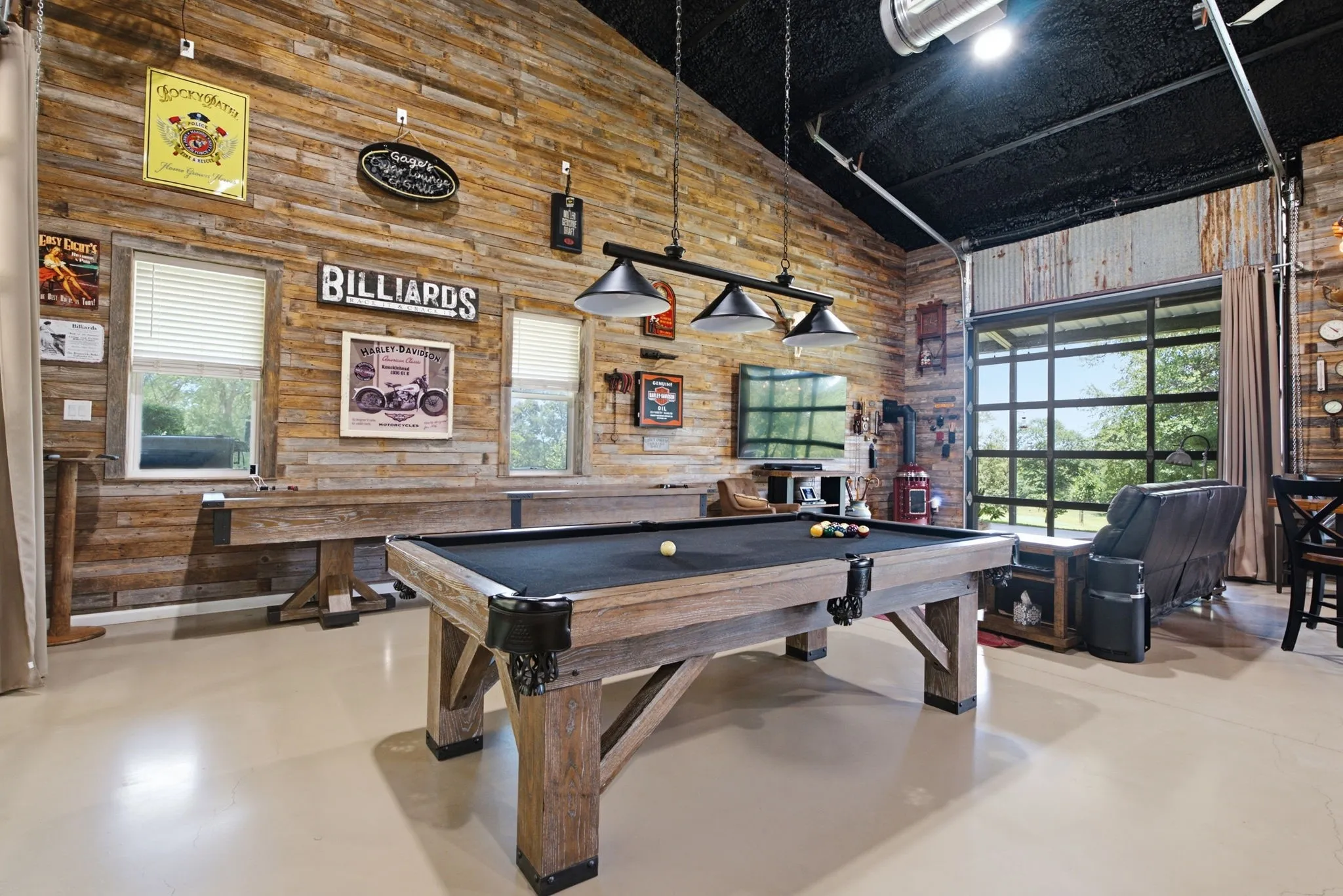 Vaulted ceiling with exposed beams, wood plank wall finishes, light-toned flooring, and a large glass garage door opening