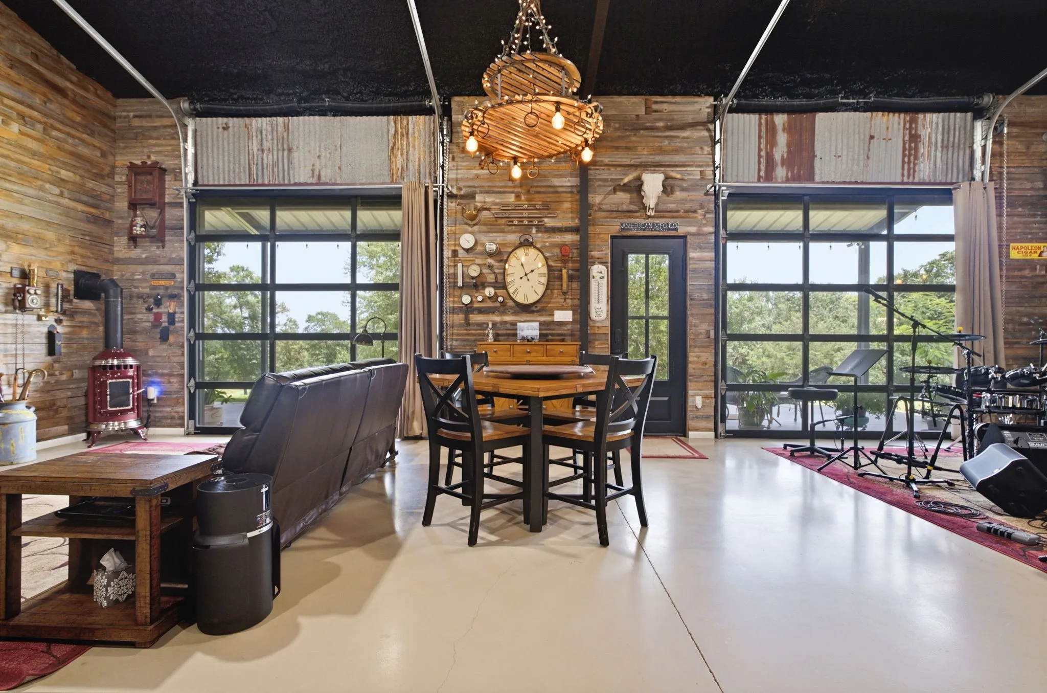 High ceilings with exposed ductwork, wood panel accent walls, large glass garage door, wood-finish flooring, and built-in wood-burning stove