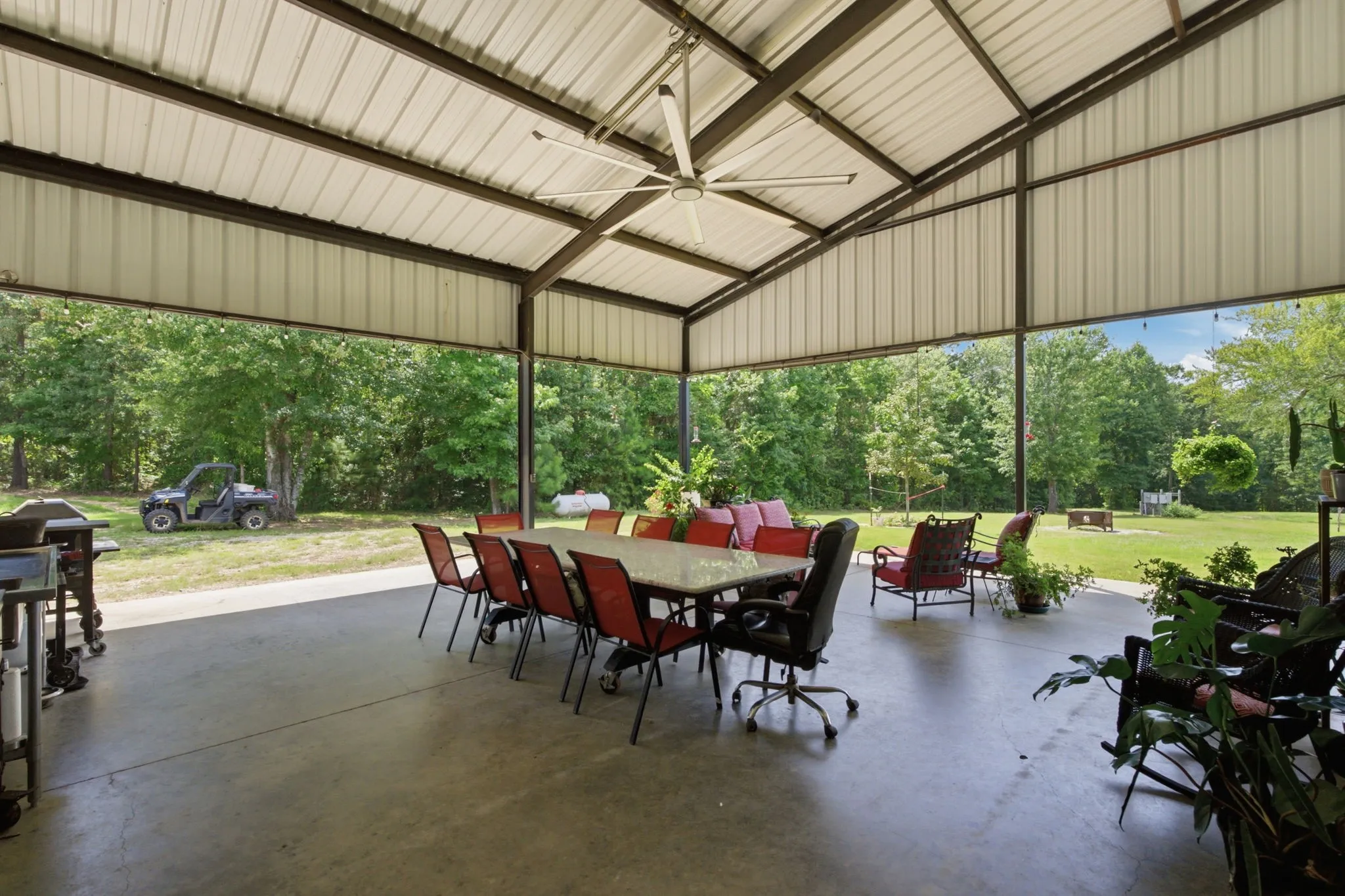 Expansive covered patio featuring a metal roof structure, concrete flooring, and a large ceiling fan