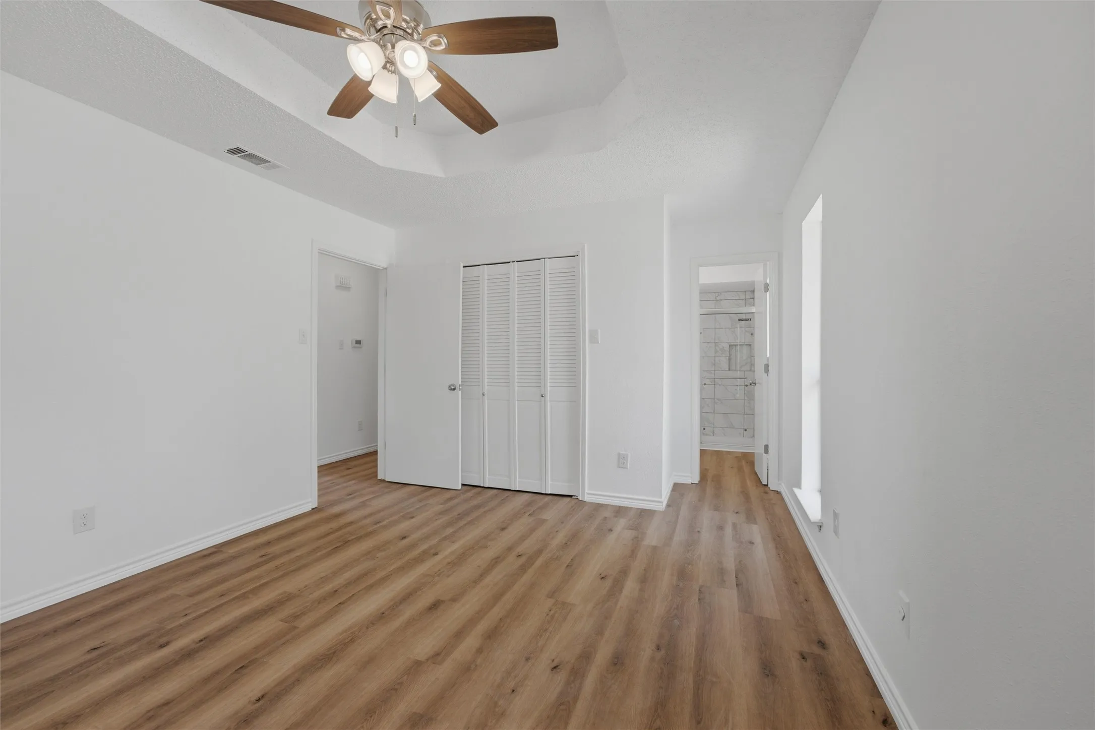 Wood-finish flooring, white walls, tray ceiling, ceiling fan, bi-fold closet doors