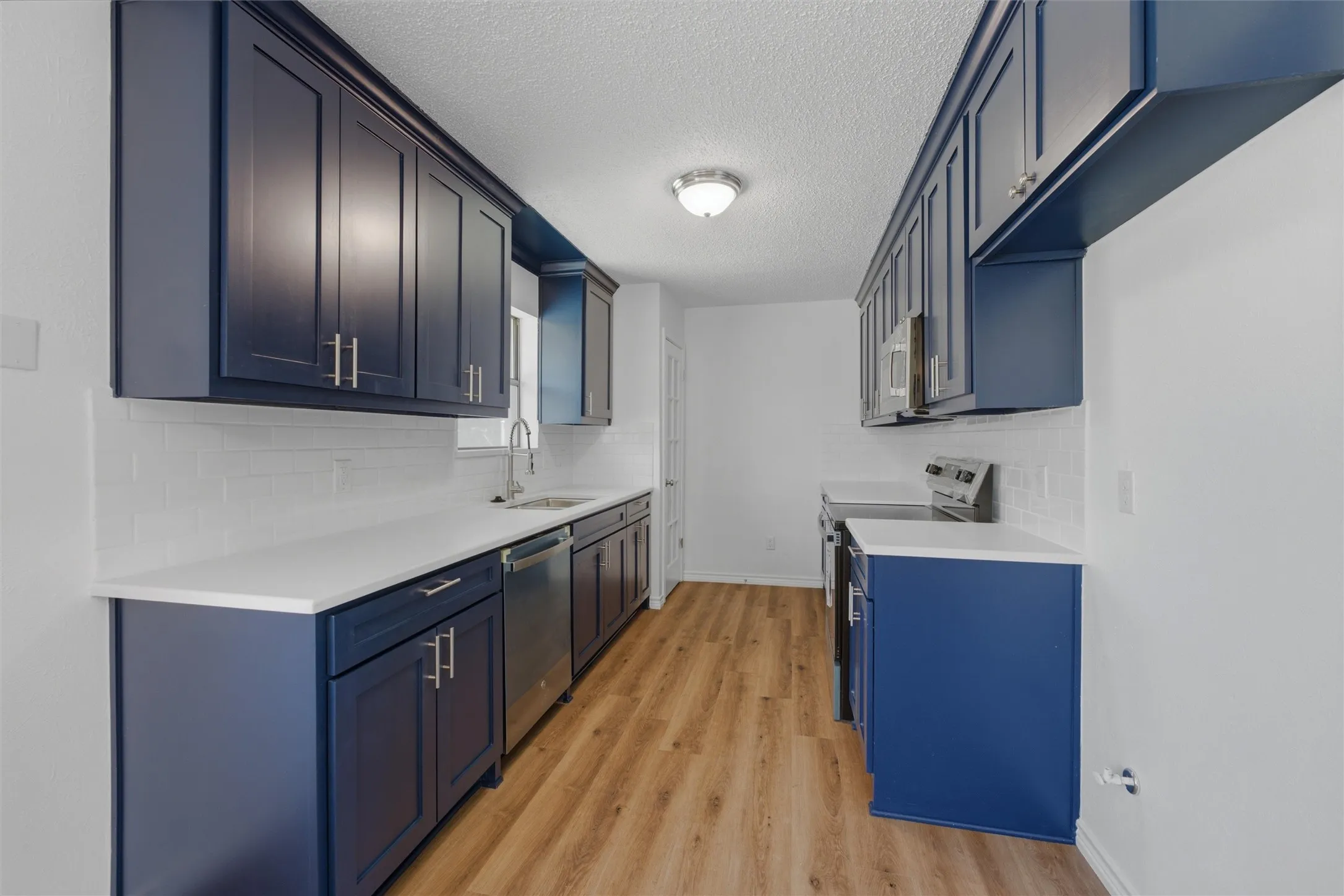 Kitchen featuring blue shaker-style cabinetry, white countertops, subway tile backsplash, stainless steel appliances, and wood-finish flooring