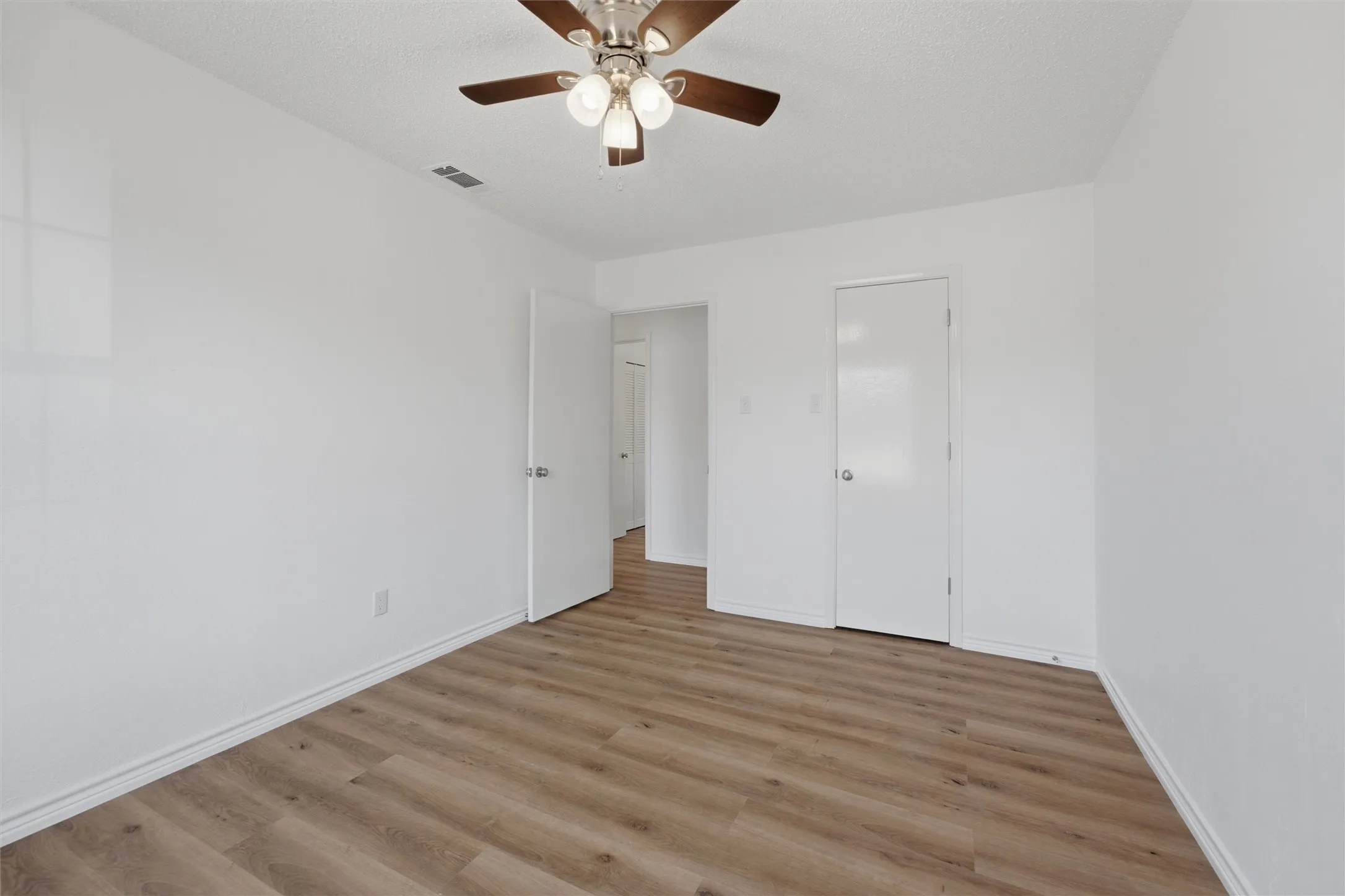 Wood-finish flooring, white walls, white doors, and a ceiling fan with light fixture