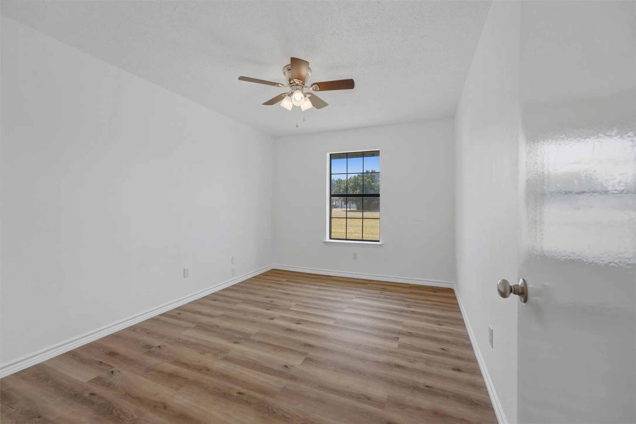 Wood-finish flooring, single window, ceiling fan with light fixture, and white walls