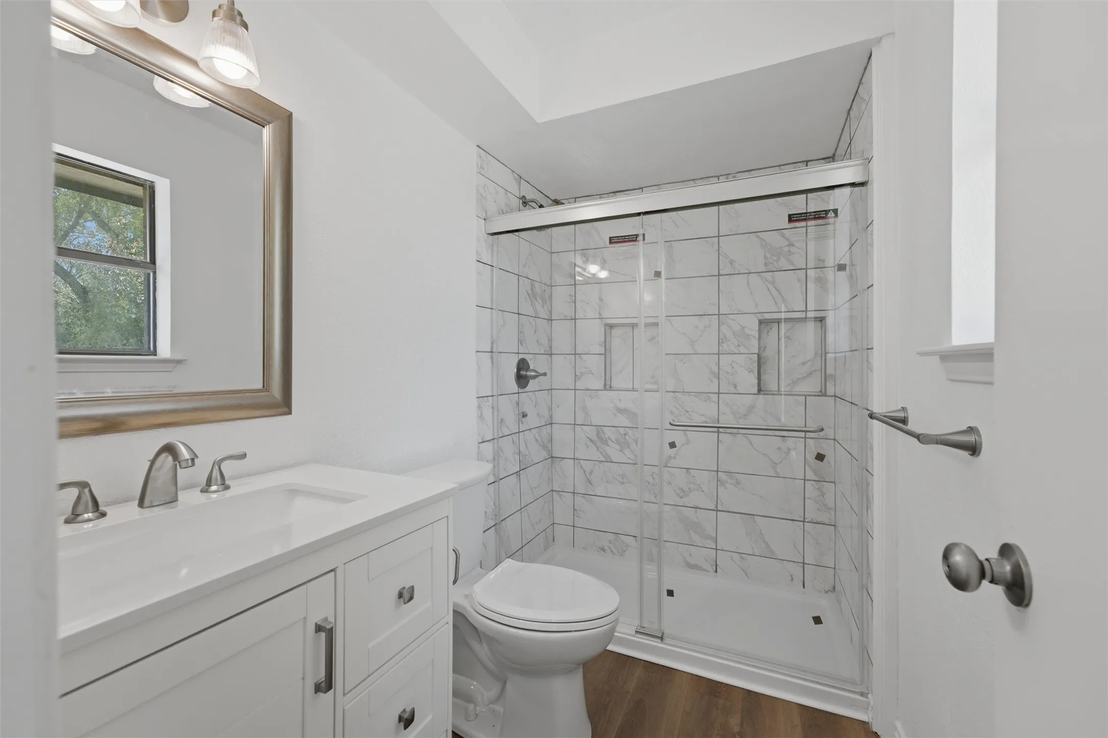 White shaker-style vanity with an integrated sink, brushed nickel hardware, and wood-finish flooring