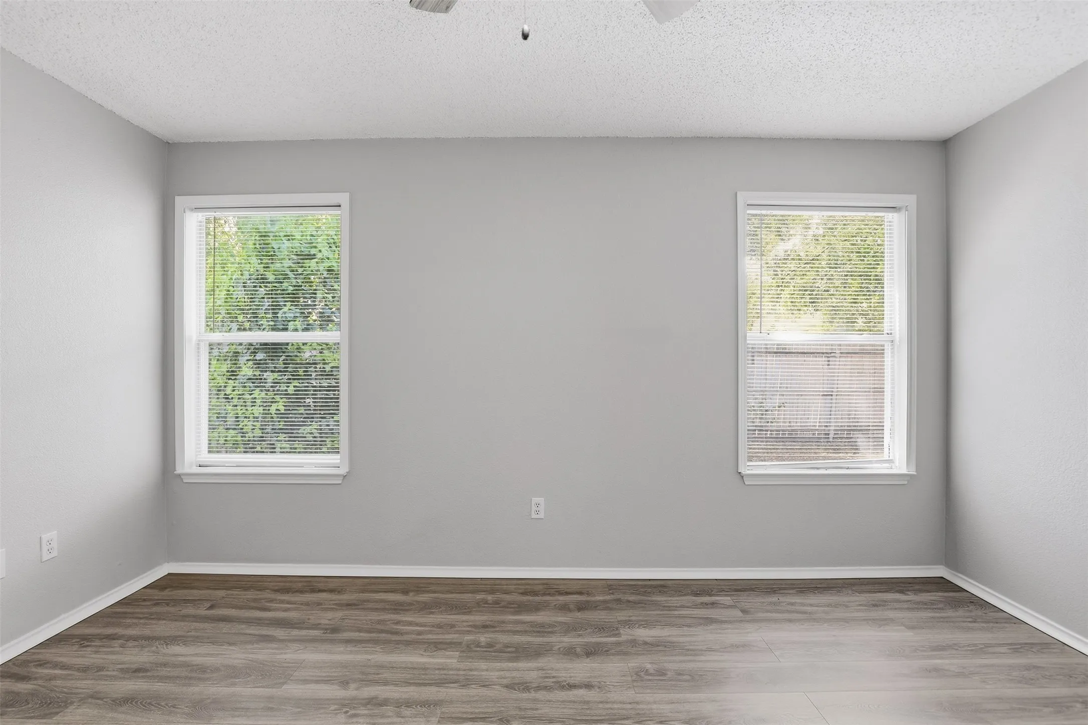 Wood-finish flooring with light gray walls, two windows, and a ceiling fan