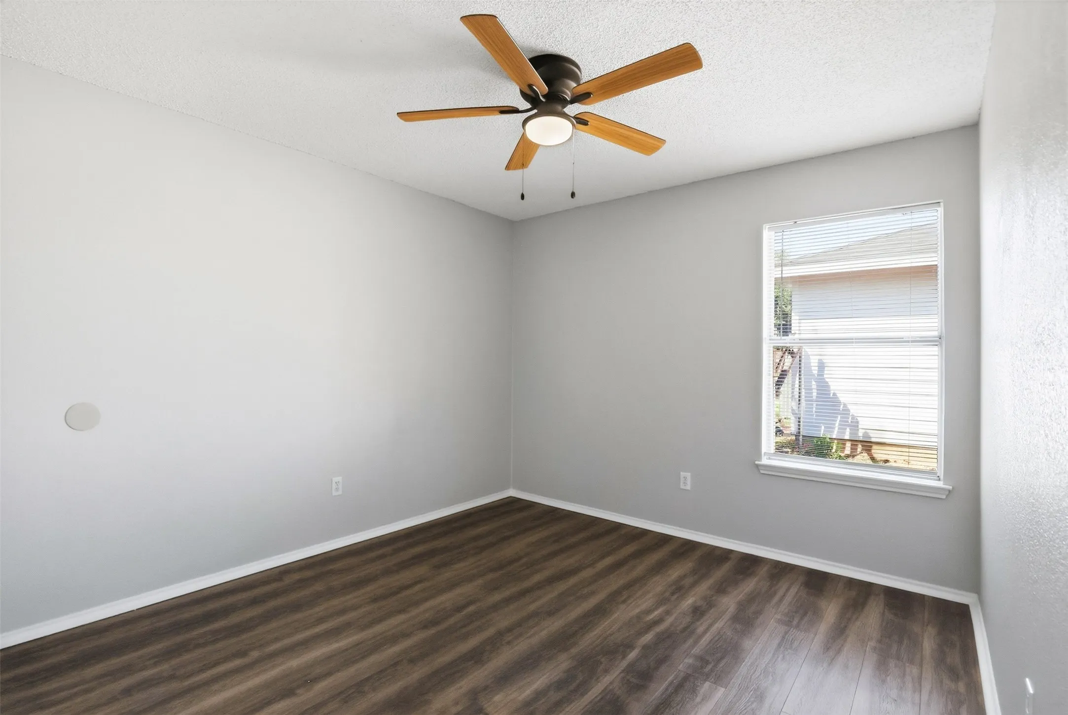 Wood-finish flooring with crisp white baseboards, a ceiling fan with light fixture, and a window with blinds