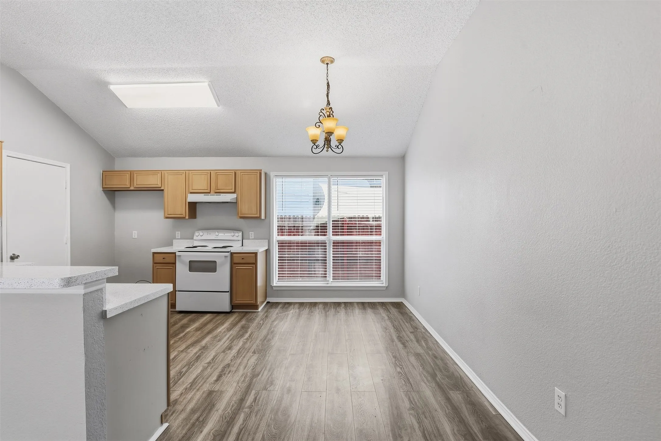 Kitchen and dining area featuring vaulted ceilings, wood-finish flooring, light wood cabinetry, a window with blinds, and an overhead chandelier