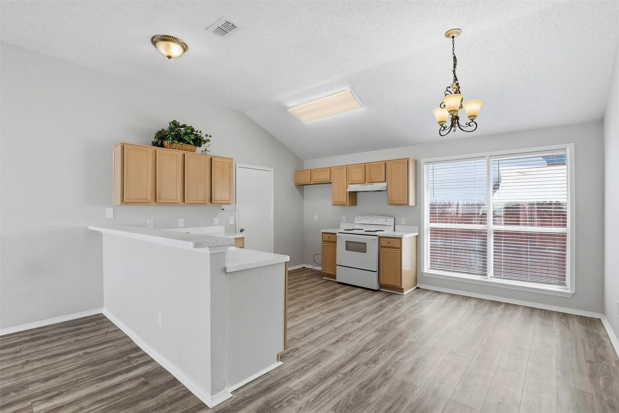 Kitchen with wood-finish flooring, vaulted ceiling, wood cabinetry, built-in range, and a breakfast bar with solid surface countertops