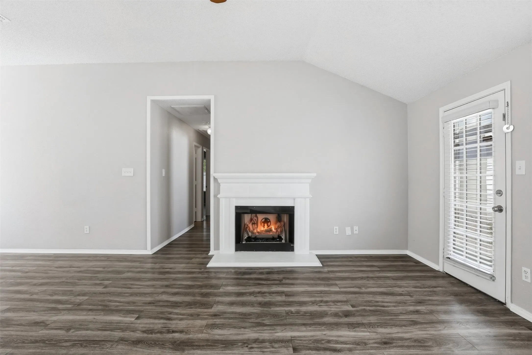 Vaulted ceiling, wood-finish flooring, white fireplace with hearth, white walls, and glass-paneled door