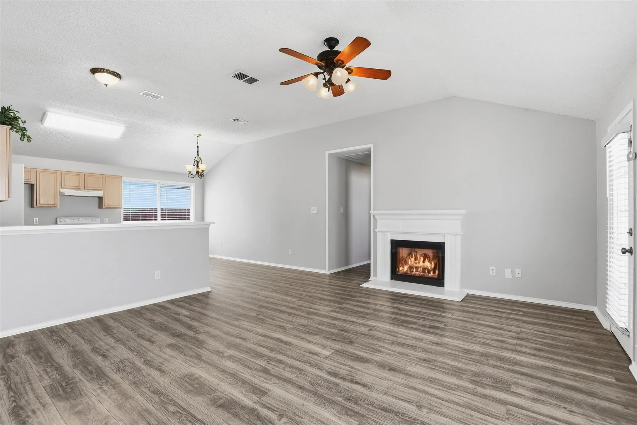 Wood-finish flooring throughout, vaulted ceiling, and a built-in decorative fireplace with white mantel