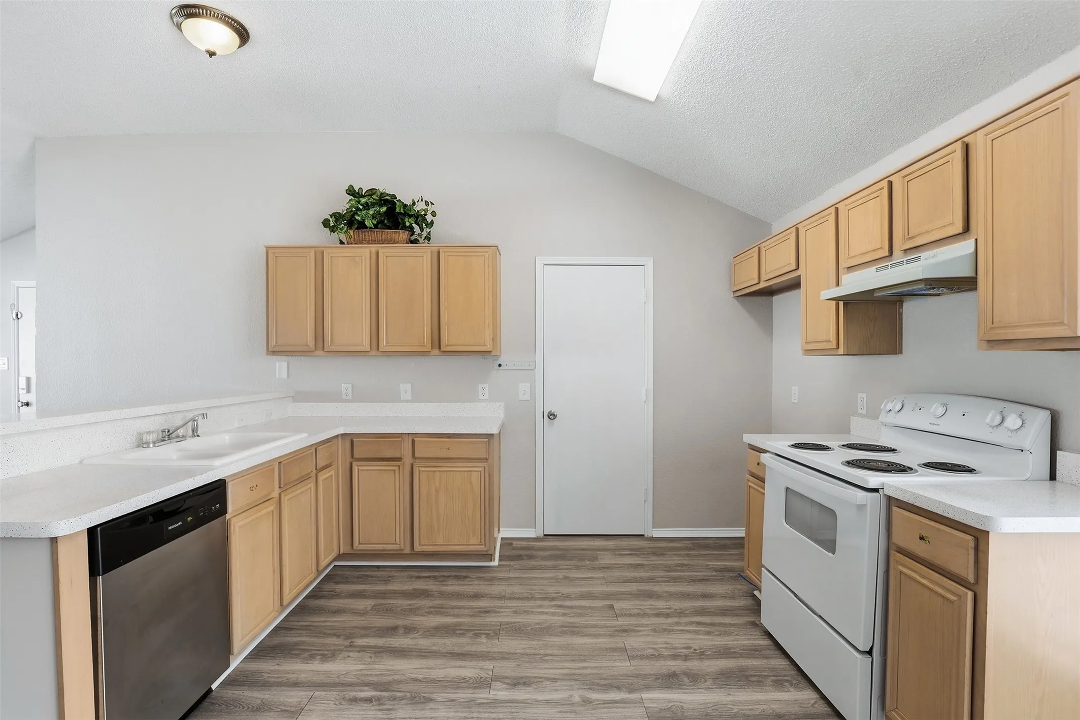 Vaulted ceiling, wood-finish flooring, wood cabinetry, white countertops, and white appliances