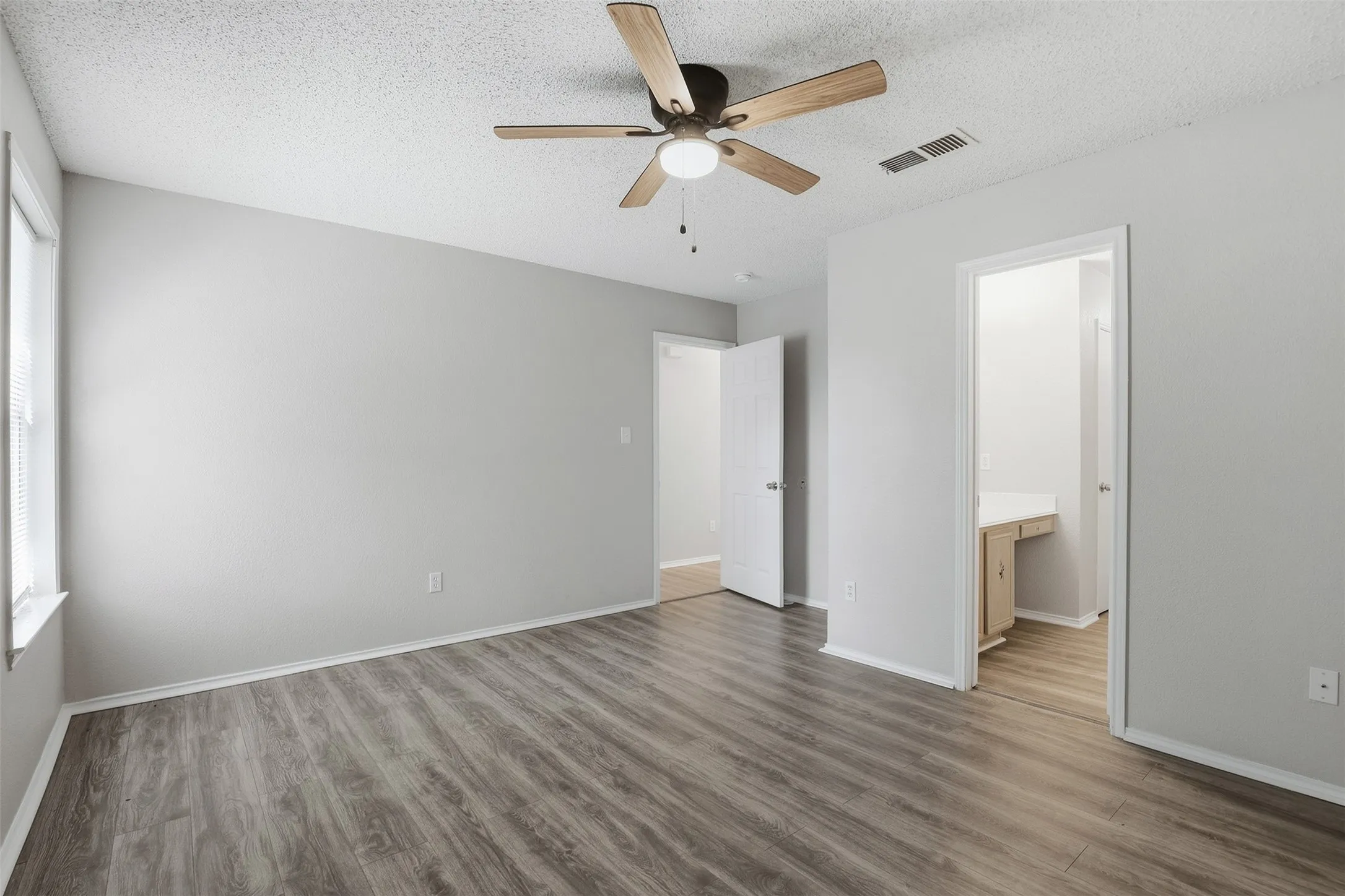Spacious room with wood-finish flooring, light gray wall paint, and a ceiling fan with light fixture