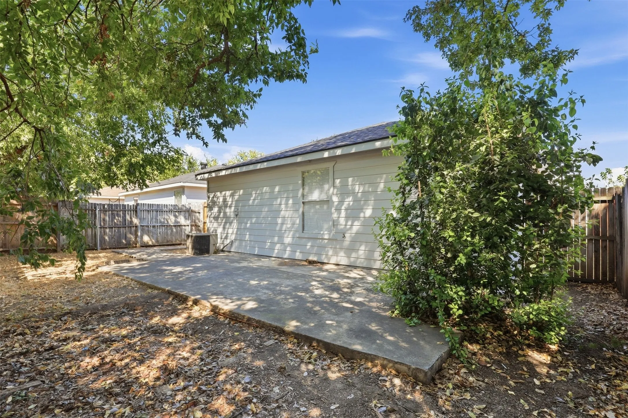 Expansive backyard featuring a concrete patio, mature trees, and a wood privacy fence