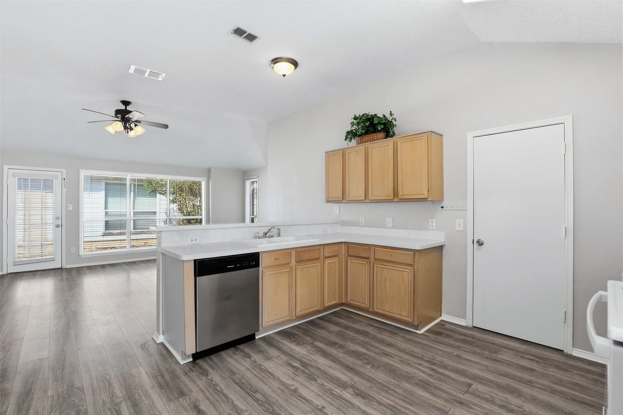 Kitchen featuring wood-finish flooring, light wood cabinetry, a stainless steel dishwasher, and a white countertop