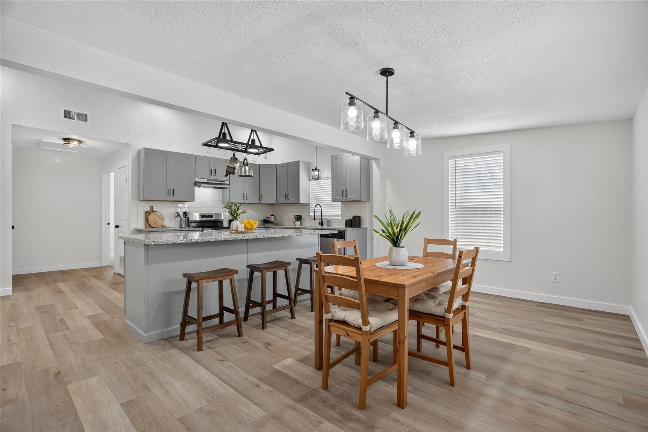 Open-concept living area featuring wood-finish flooring, a kitchen island with seating, grey cabinetry, stainless steel appliances, and a modern dining light fixture