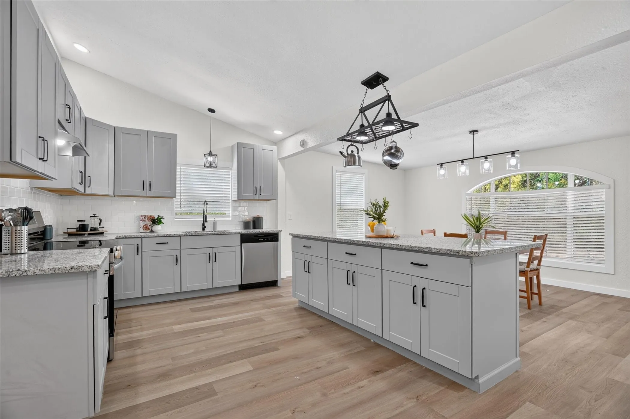 Kitchen featuring wood-finish flooring, light gray cabinetry with dark hardware, a center island with a speckled countertop, and a dining area with an arched window