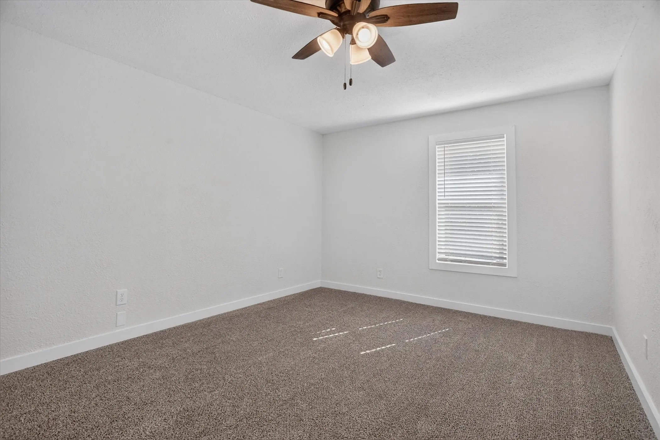 Neutral wall tones, textured ceiling, window with horizontal blinds, ceiling fan with integrated lighting, and carpeted flooring