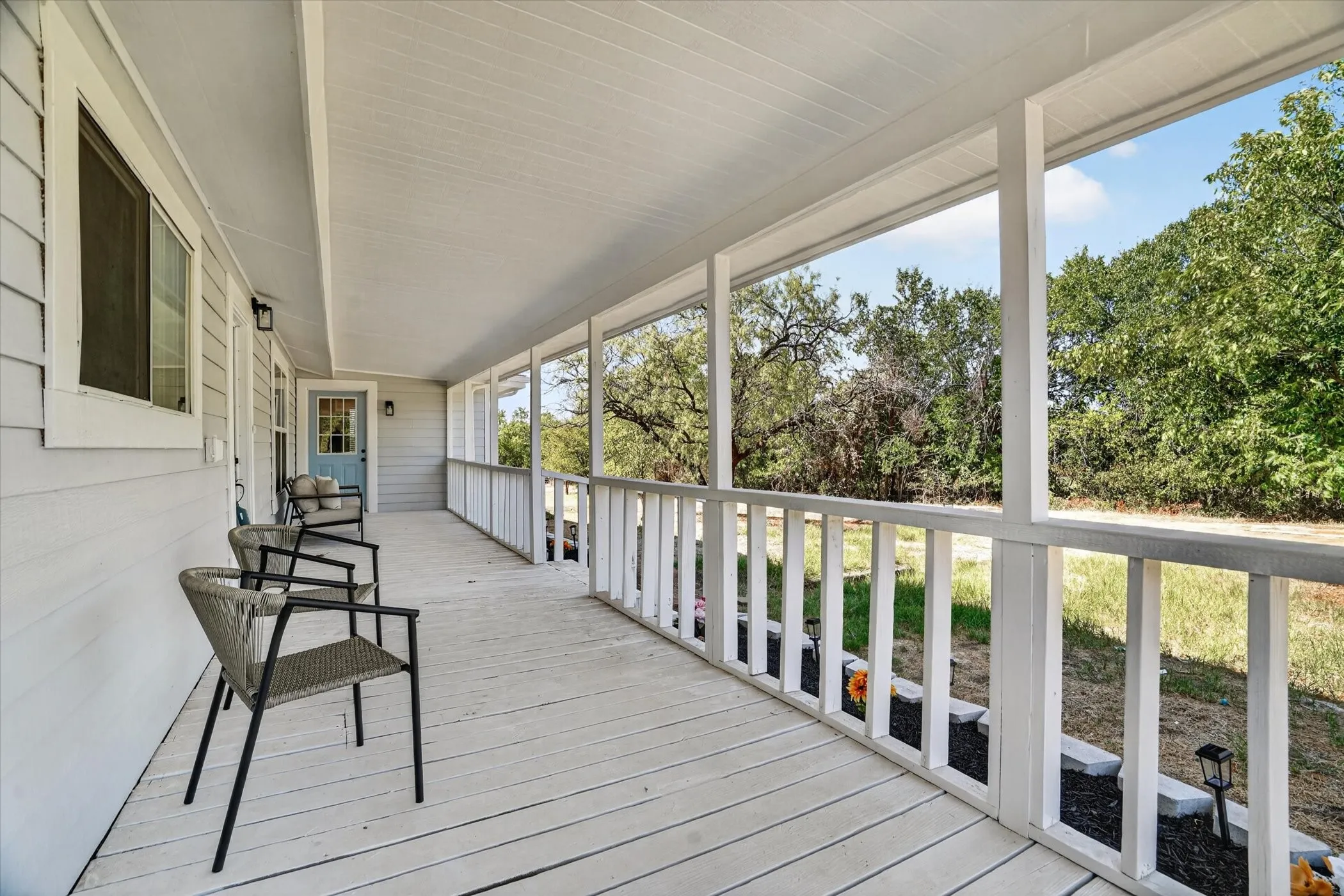Expansive covered porch with wood-finish flooring, white railing, and a light blue entry door