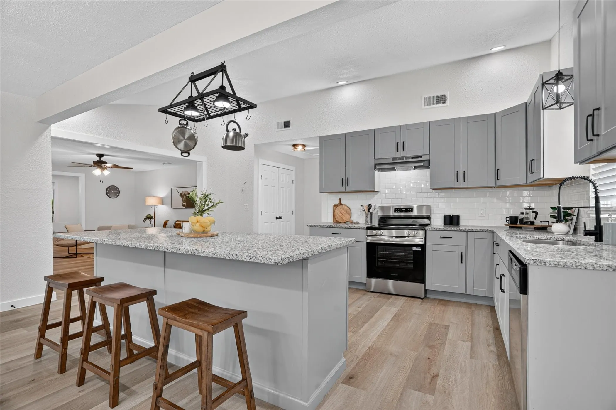 Kitchen featuring an island with a light-toned countertop, gray cabinetry, stainless steel appliances, wood-finish flooring, and a subway tile backsplash