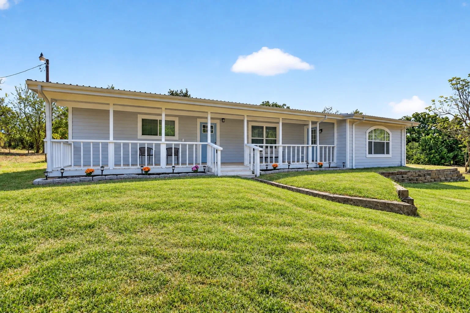 Single-story residence featuring light gray siding with white trim, a covered front porch with white railings, and a light blue front door