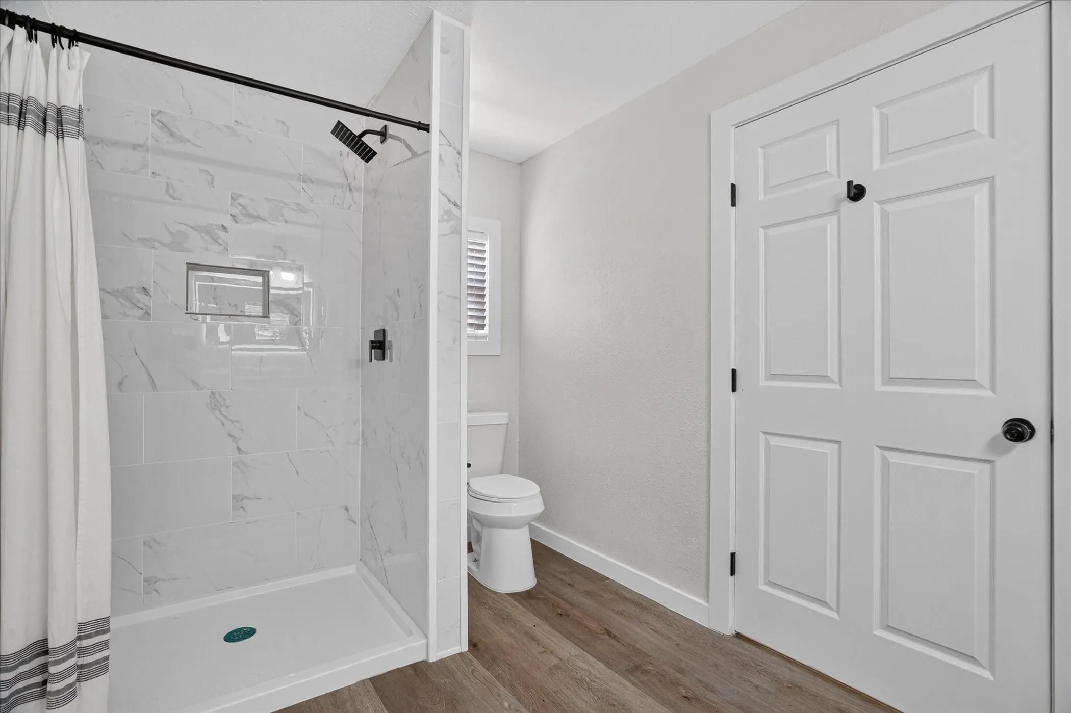 Shower with marble-look tile, matte black fixtures, and built-in niche
