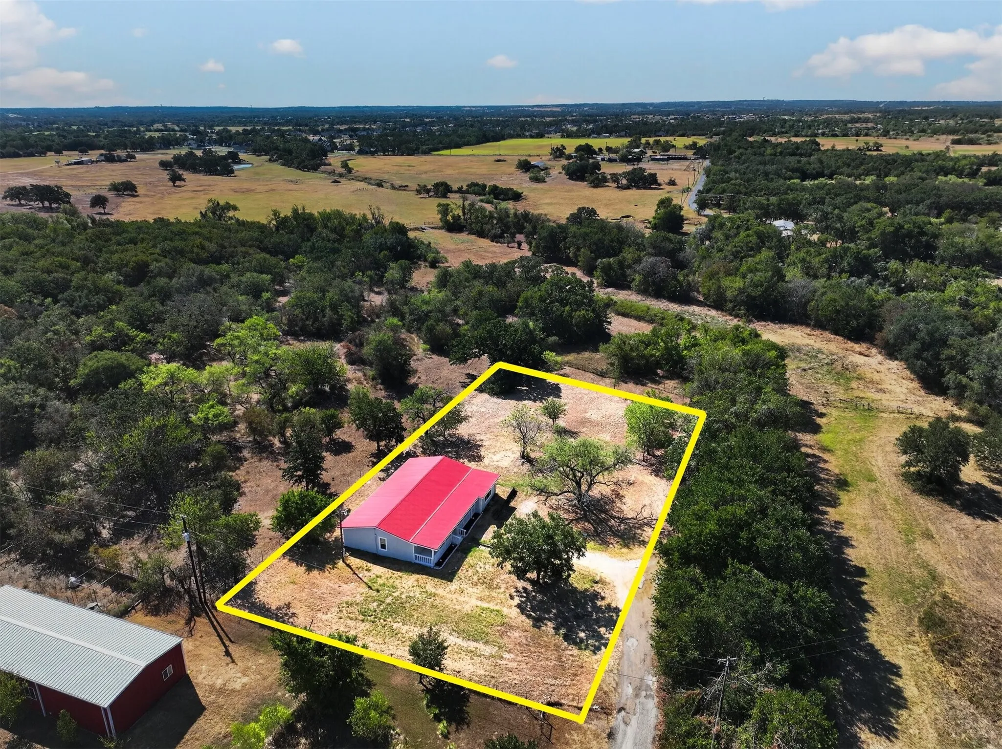 Aerial perspective showcasing a single-story residence with a red metal roof and light-colored siding