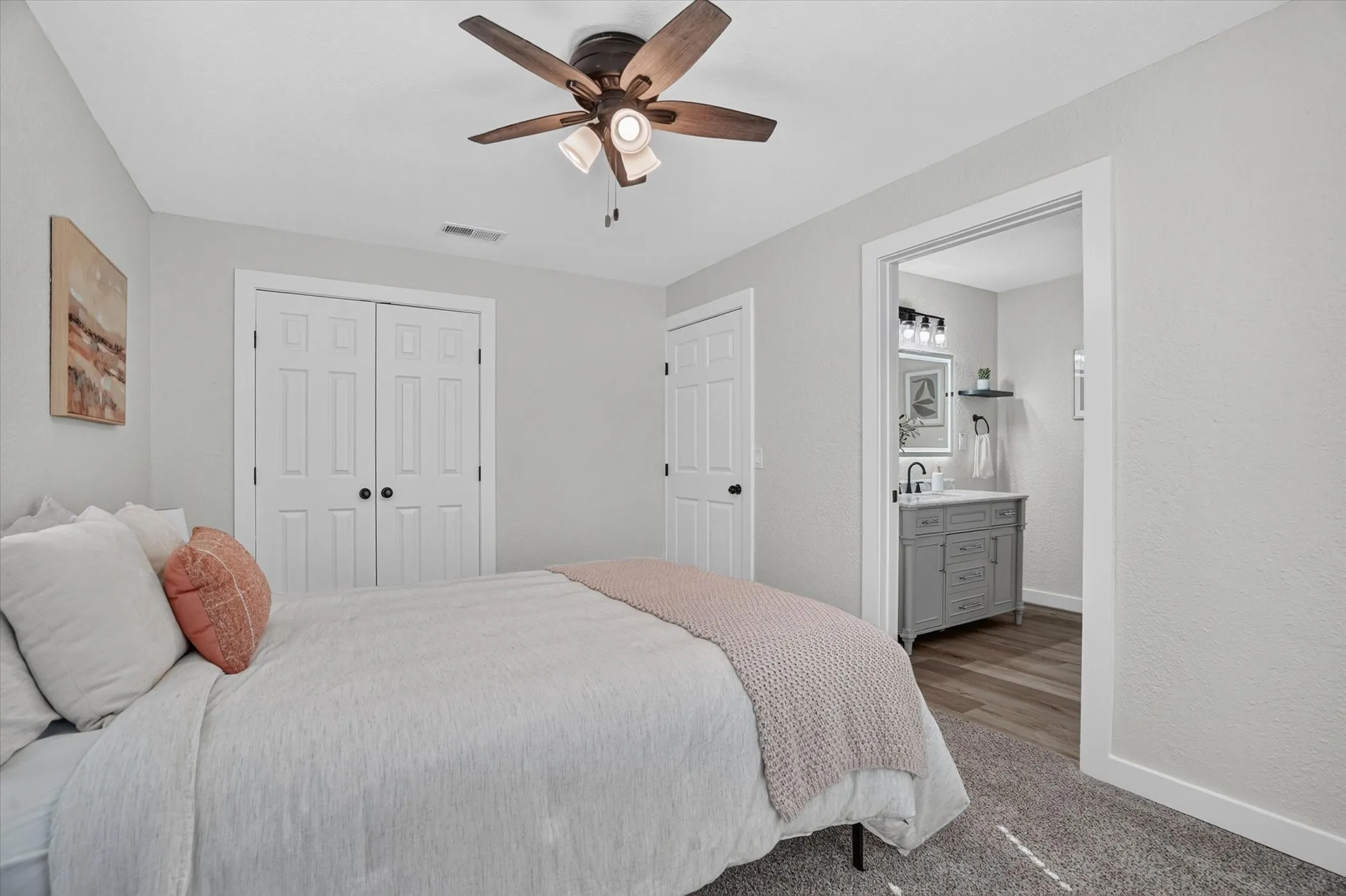 Ceiling fan with integrated lighting, dual bifold closet doors, light gray wall finish, and an adjacent bathroom with a vanity sink