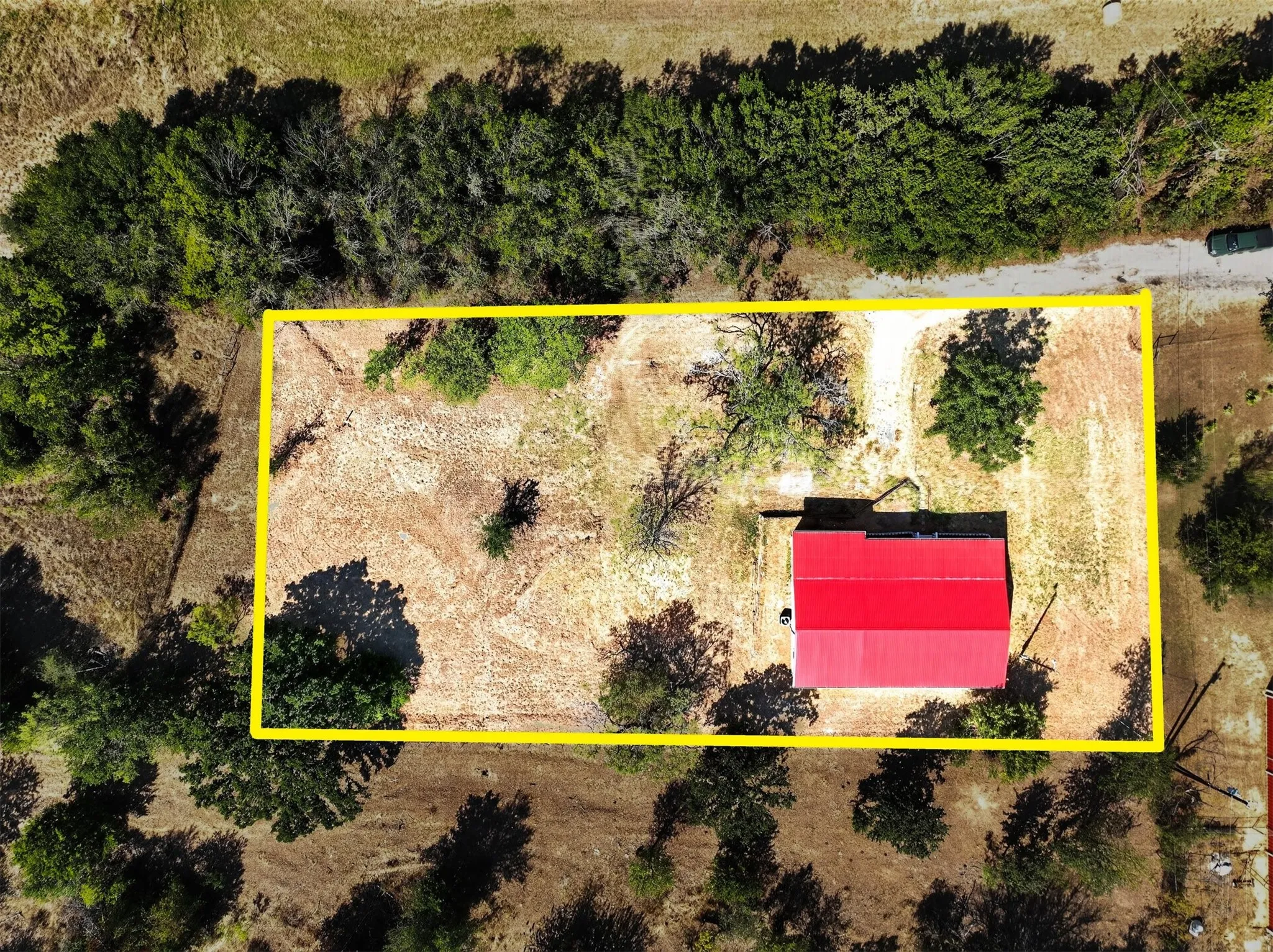 Property boundary featuring a structure with a red roof, surrounded by varied foliage and a natural landscape