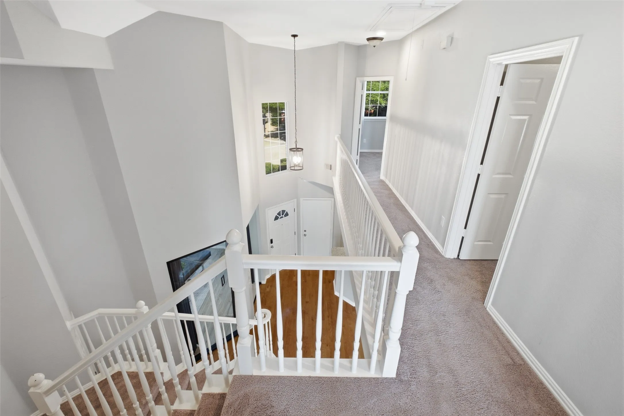 The upstairs landing overlooks the staircase and two-story entry, with a pendant lantern casting a warm glow over the wide carpeted hallway. Bedroom and bath doors line the hall, giving each room its own defined space and privacy.