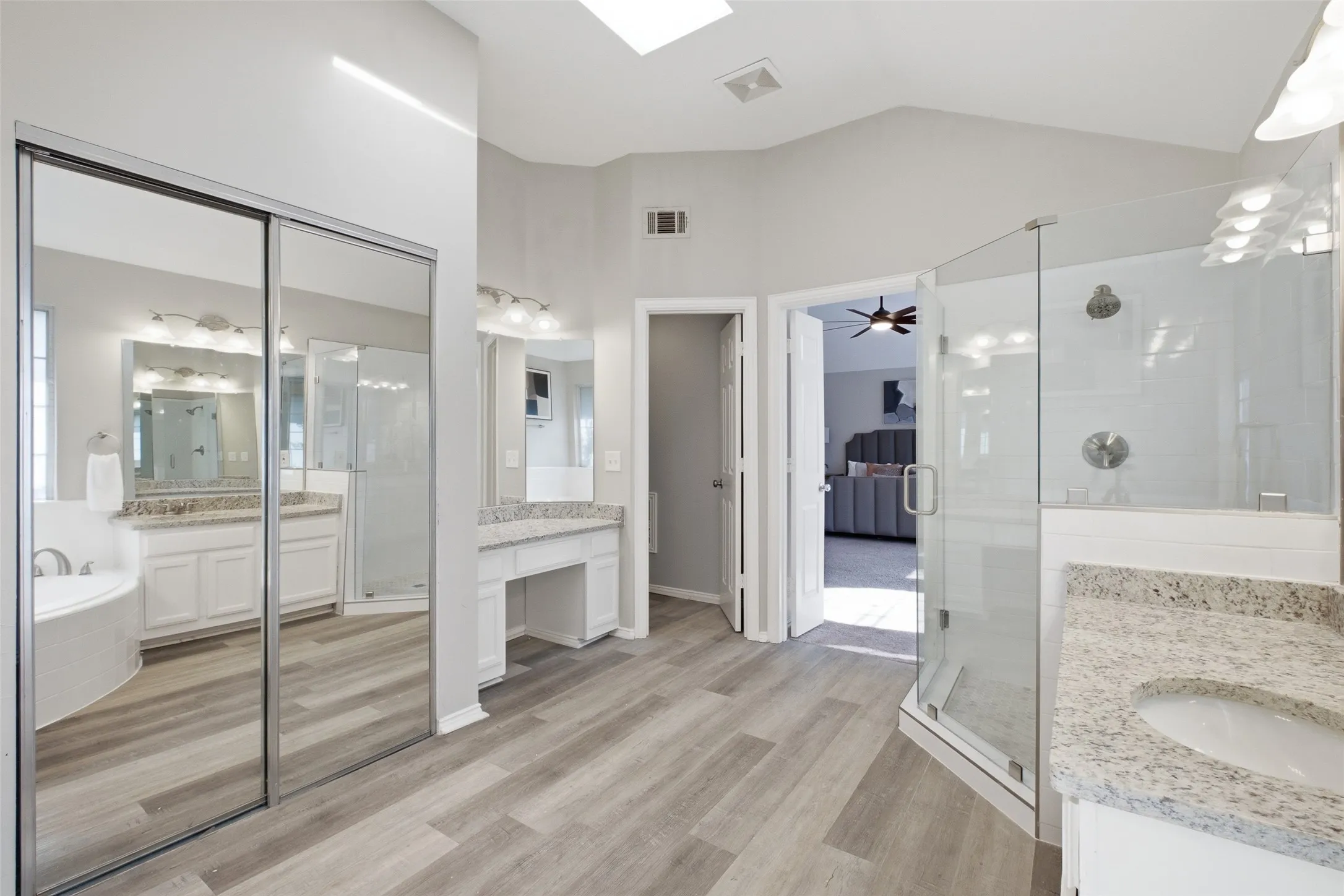 Floor-to-ceiling mirrored closet doors, a built-in makeup vanity station, and a vaulted ceiling with skylight make this primary bathroom feel expansive and bright. Every detail — from the granite counters to the walk-in shower — has been designed with comfort and function in mind.