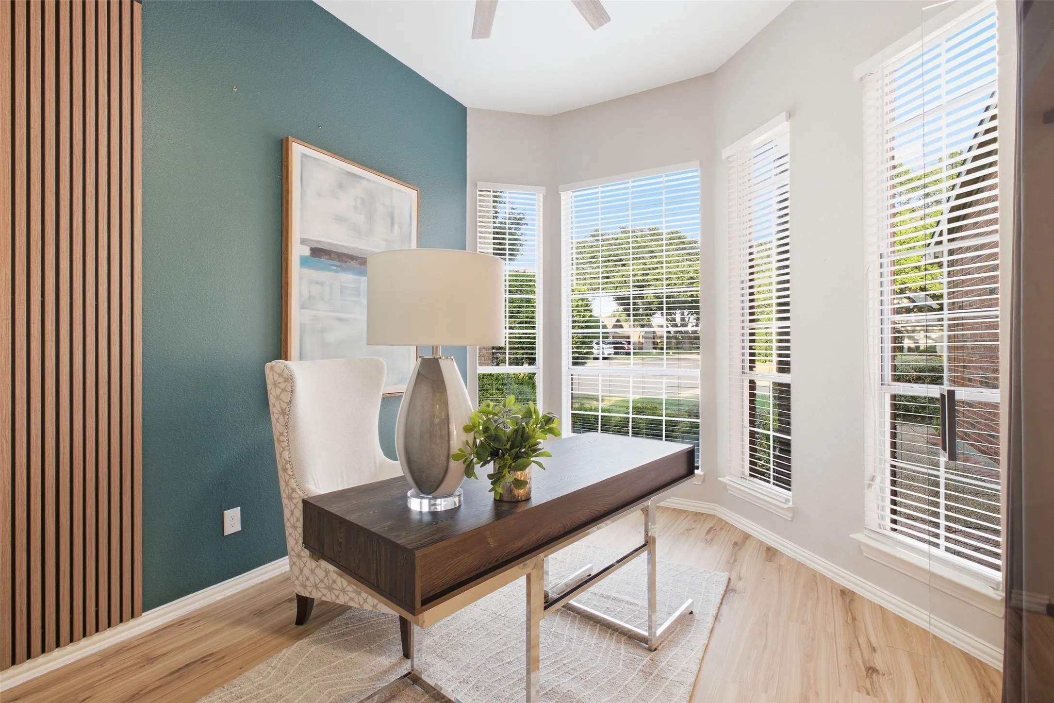 A statement teal accent wall paired with a warm wood slat panel creates a dynamic backdrop for this stylish main-level office. Bay windows overlook the front of the home and fill the space with light, while wood-look flooring and a glass barn door add a polished, modern edge.