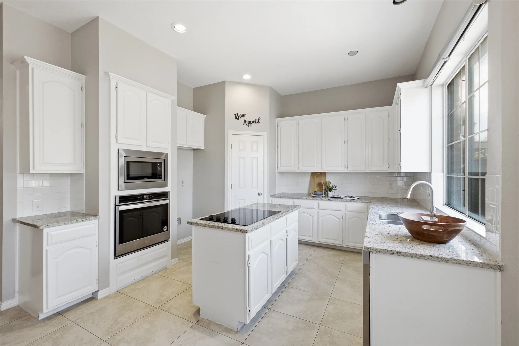 Double wall ovens, a built-in microwave, and an island cooktop make this kitchen a serious cook's dream. White cabinetry runs floor to ceiling on the appliance wall for maximum storage, while granite counters wrap the entire perimeter and island.
